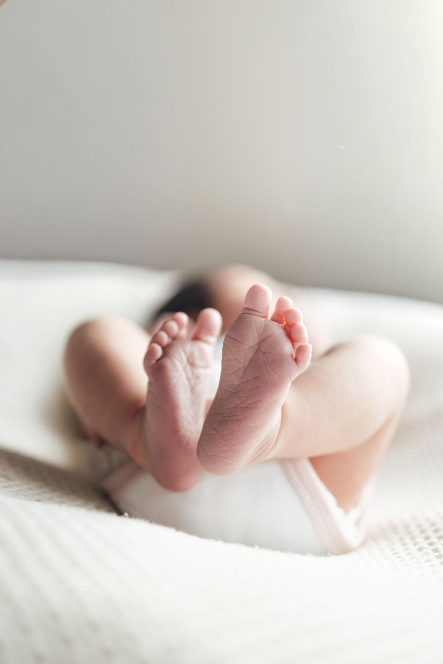 Close-up of tiny newborn baby feet resting on a soft white blanket in natural light.