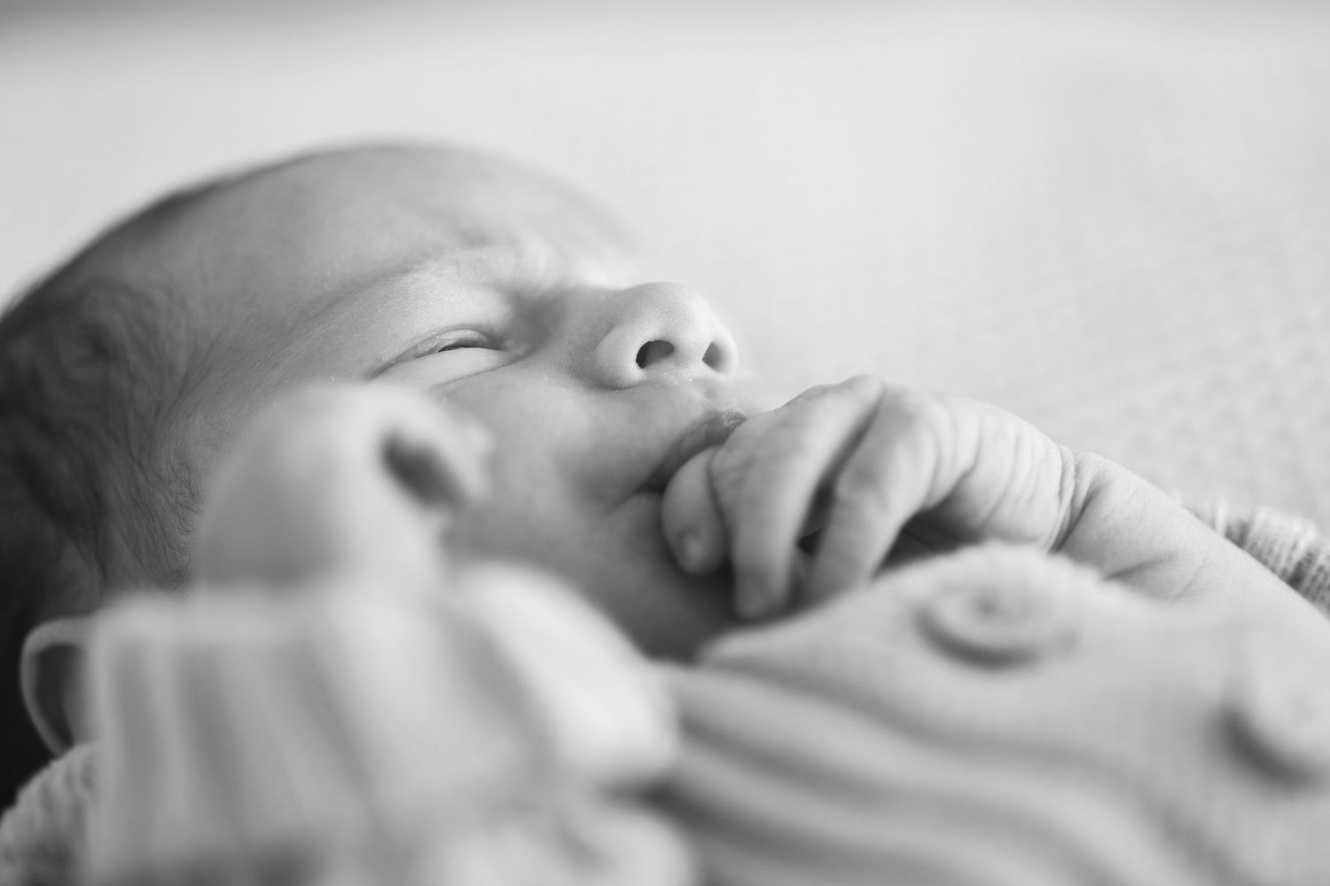 Peaceful sleeping newborn baby in black and white, hands tucked near face wearing soft knit mittens.