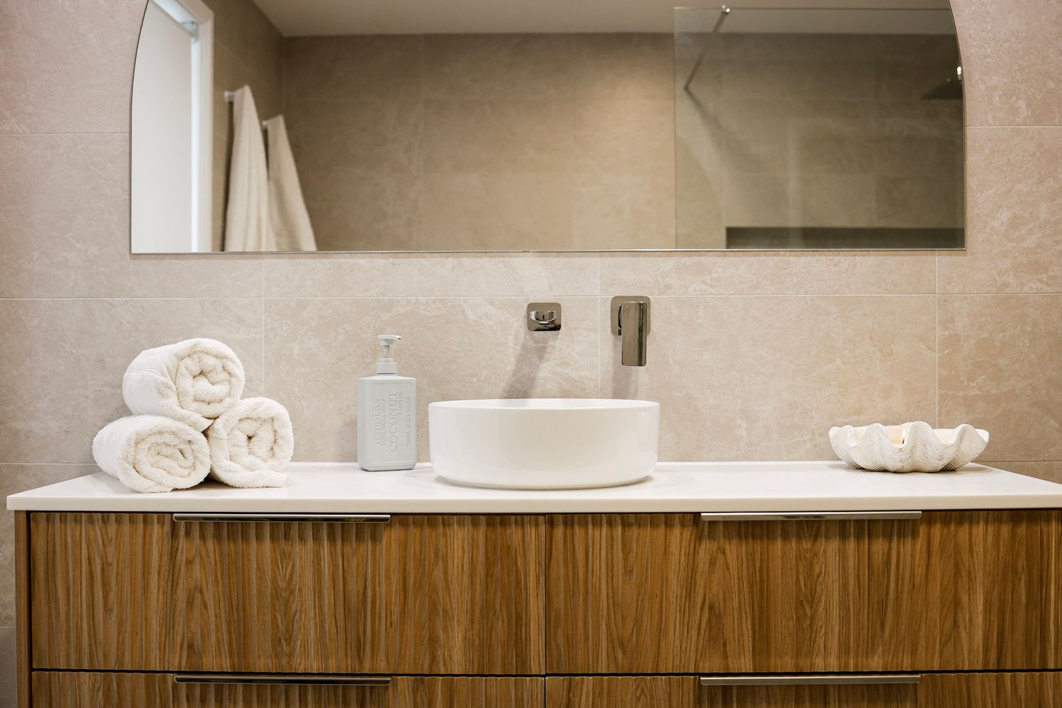 Modern bathroom vanity with white vessel sink, rolled towels and wood cabinetry.