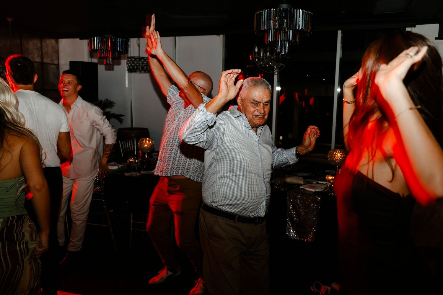 Older gentleman dancing energetically with arms raised at a lively wedding reception party.