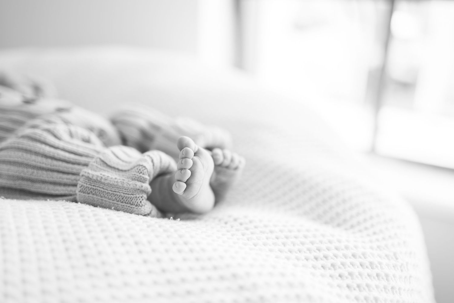 Close-up black and white photo of newborn baby feet wrapped in a knit blanket resting on a white surface.