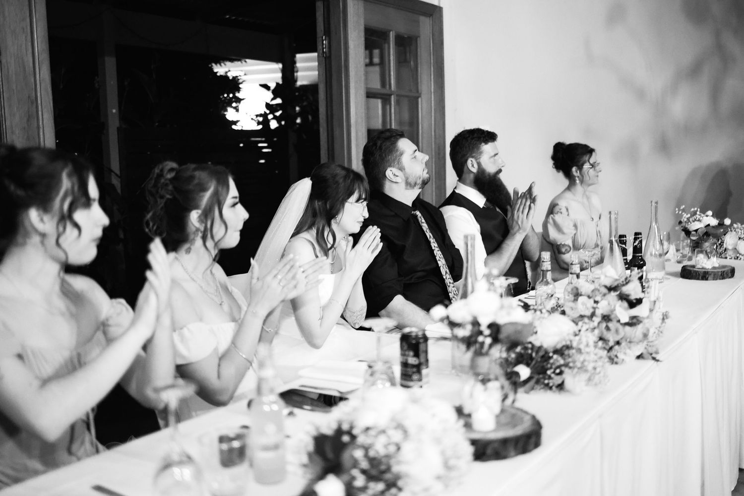 Wedding party clapping and celebrating at the head table during a elegant black and white reception.