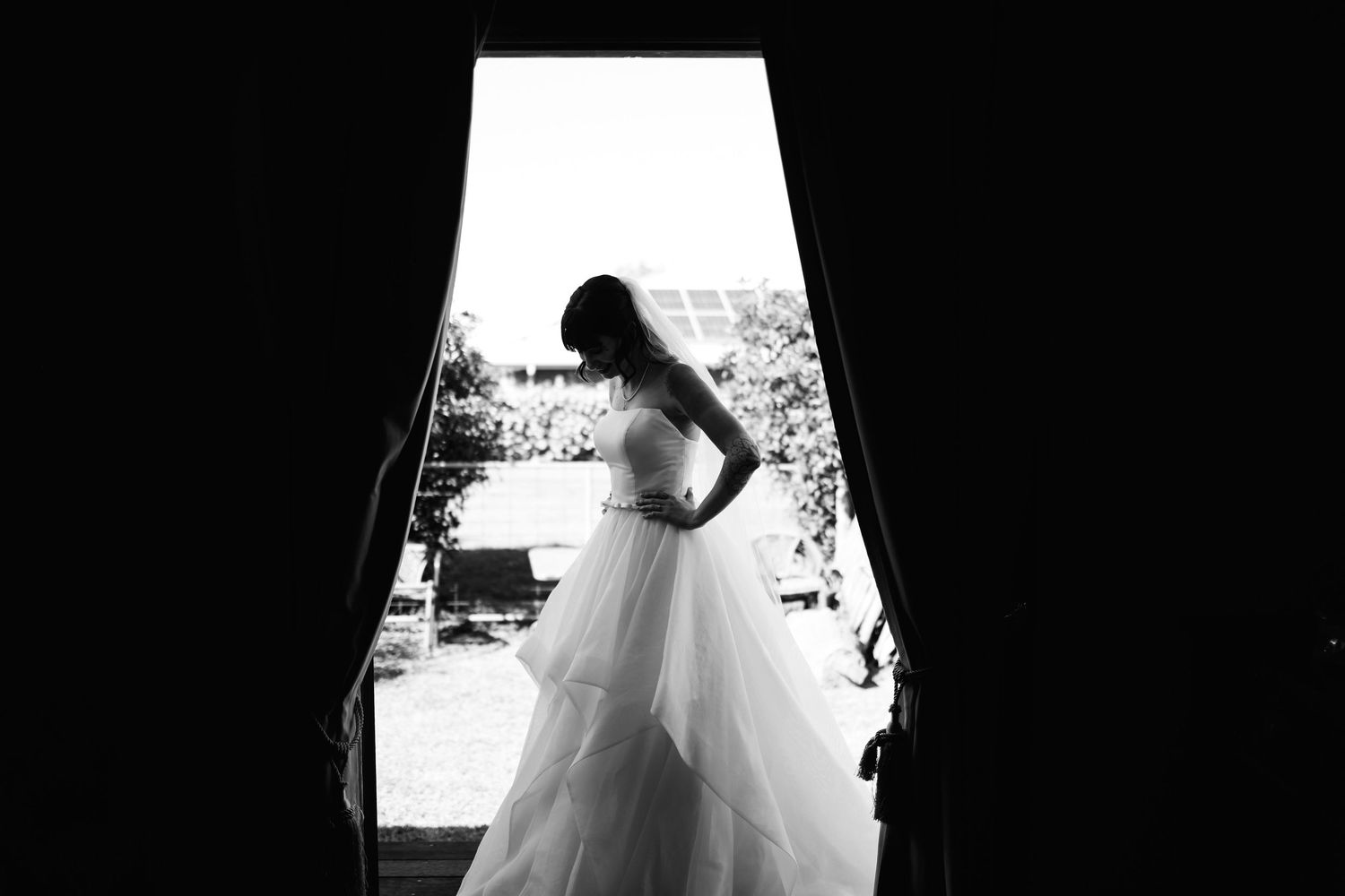 Elegant bride in a flowing ball gown silhouetted in a doorway with natural light behind her.