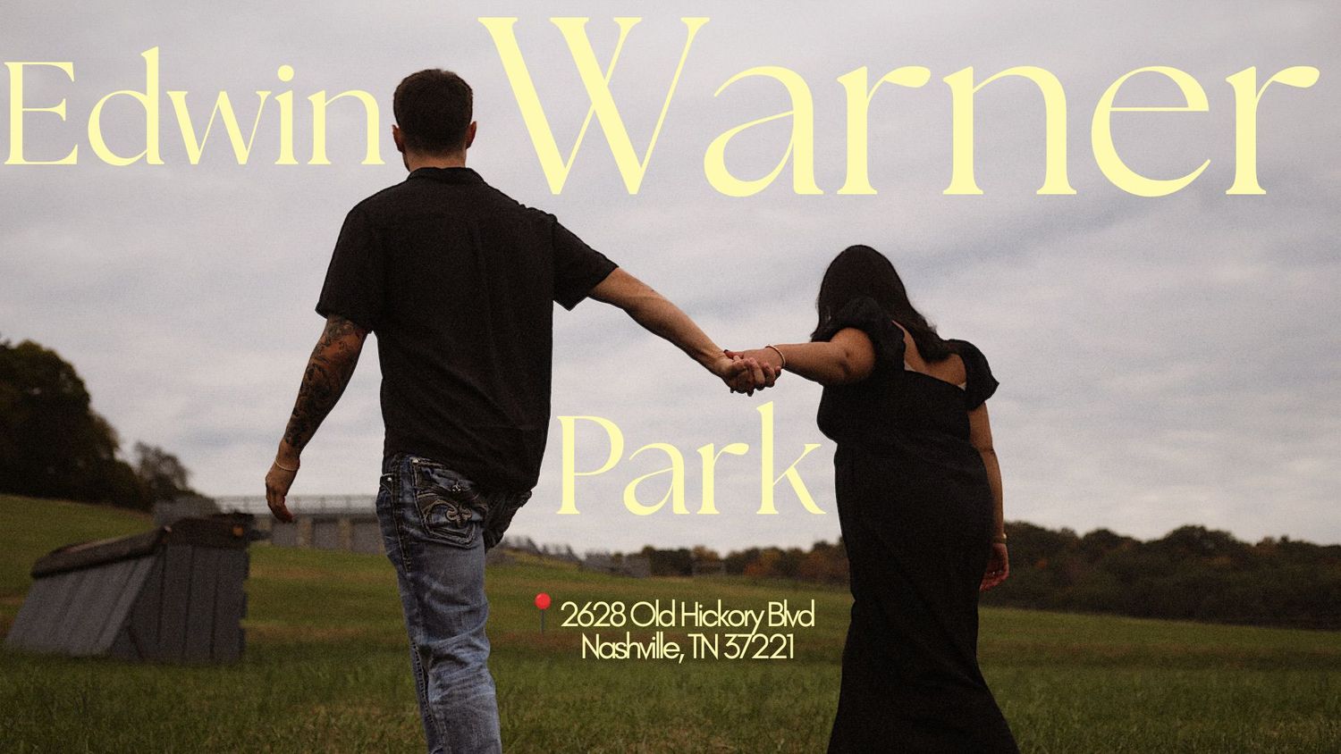 Couple holding hands walking through Edwin Warner Park in Nashville, TN, with lush green fields and trees in the background.