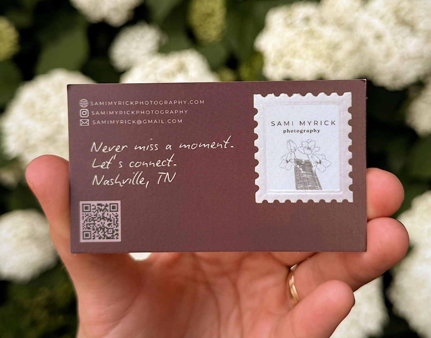 Hand holding a brown business card for Sami Myrick Photography with Nashville, TN contact details and QR code.