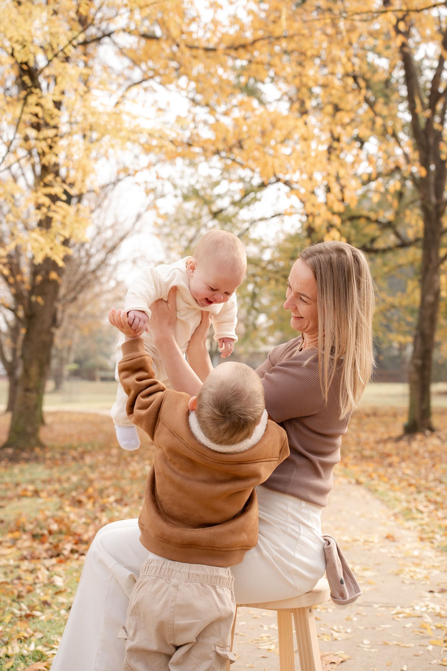 Mum and toddler looking at younger baby laughing together during motherhood photoshoot in a park in Barooga