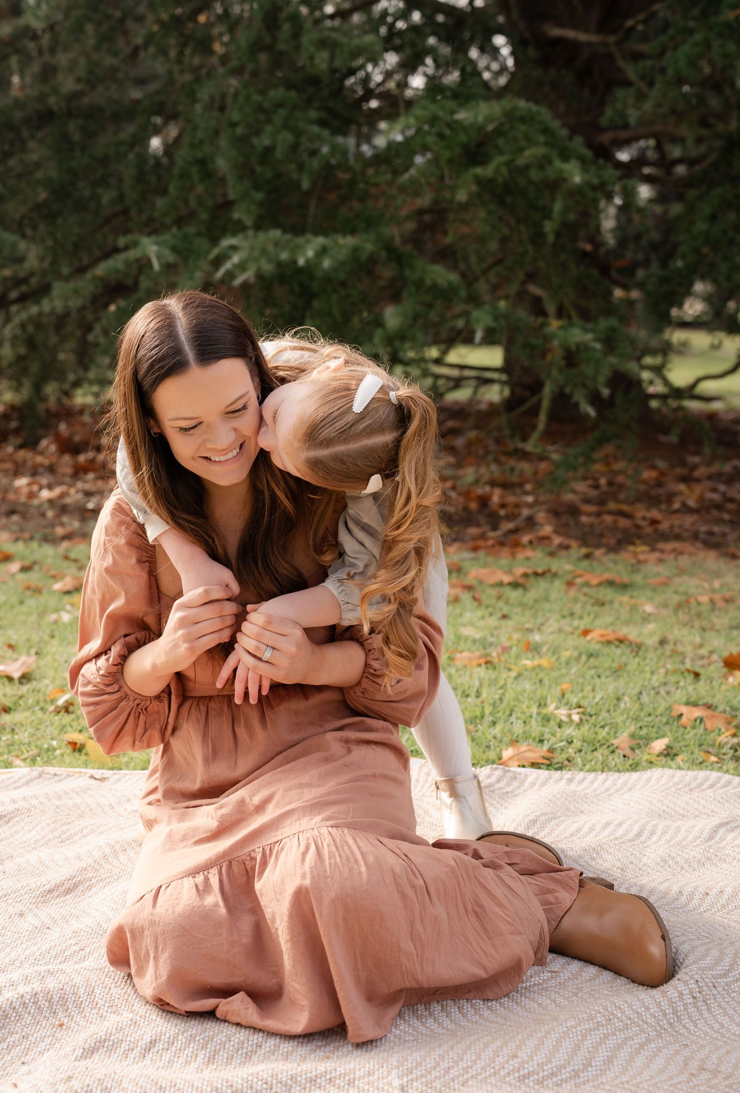 Toddler giving mum a cuddle and kiss during motherhood photoshoot sitting on the grass in a park in Barooga