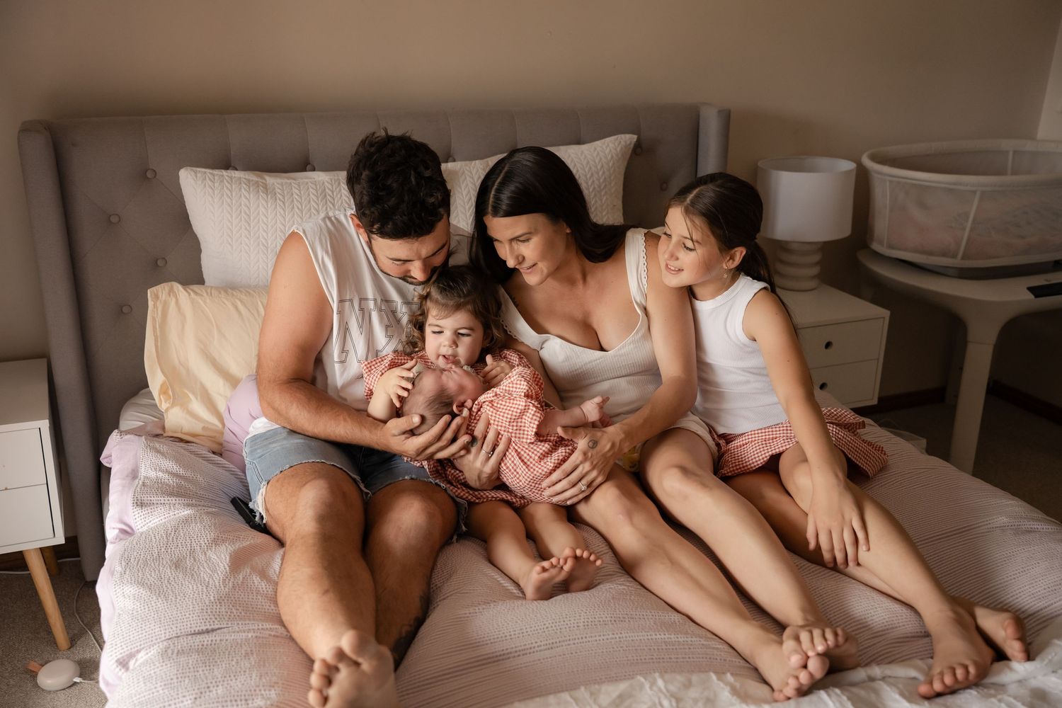 Mum and dad with three children snuggled up on a bed with their newborn during a in home newborn photoshoot in Berrigan