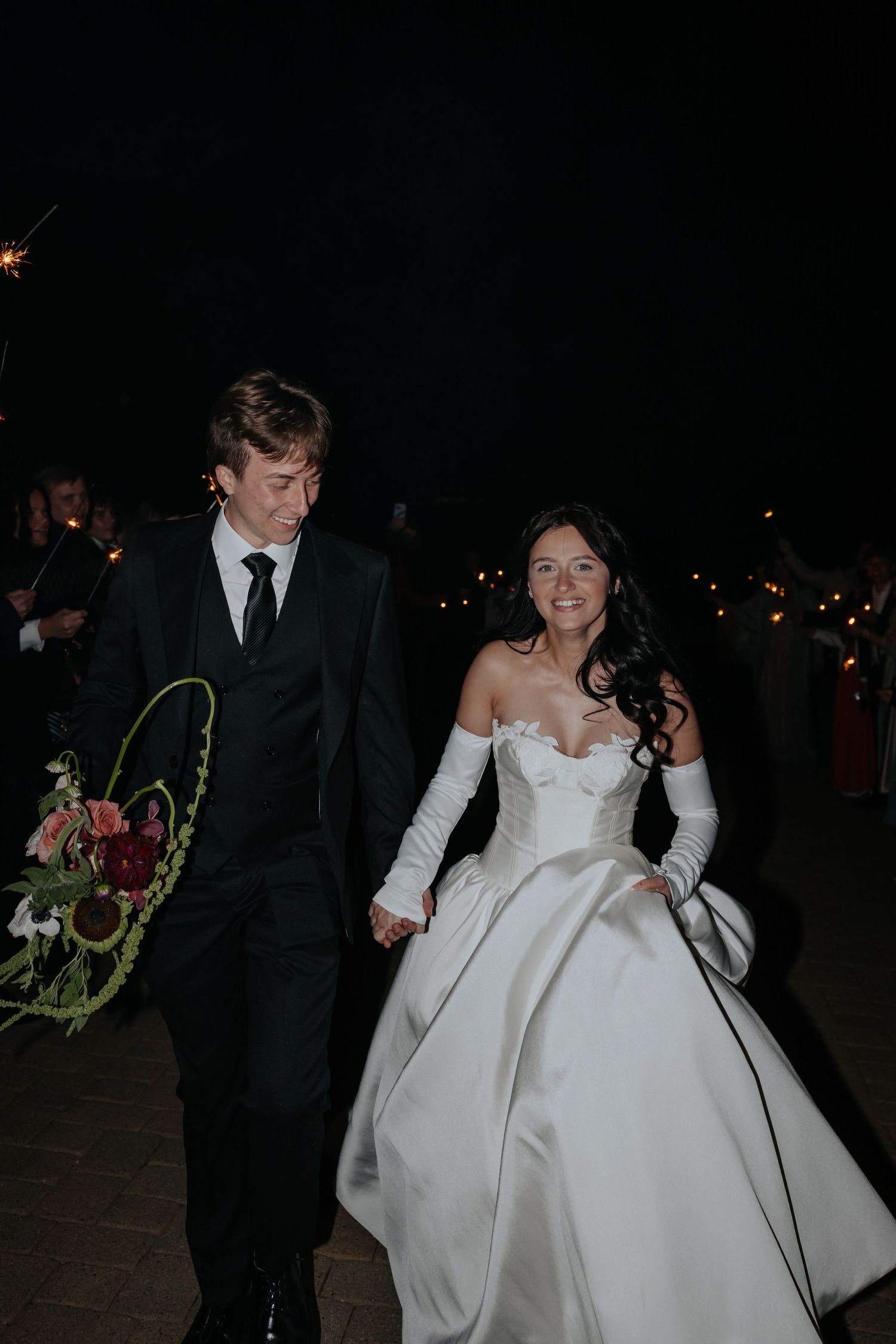 Bride and groom walking through sparkler exit at night wedding reception.