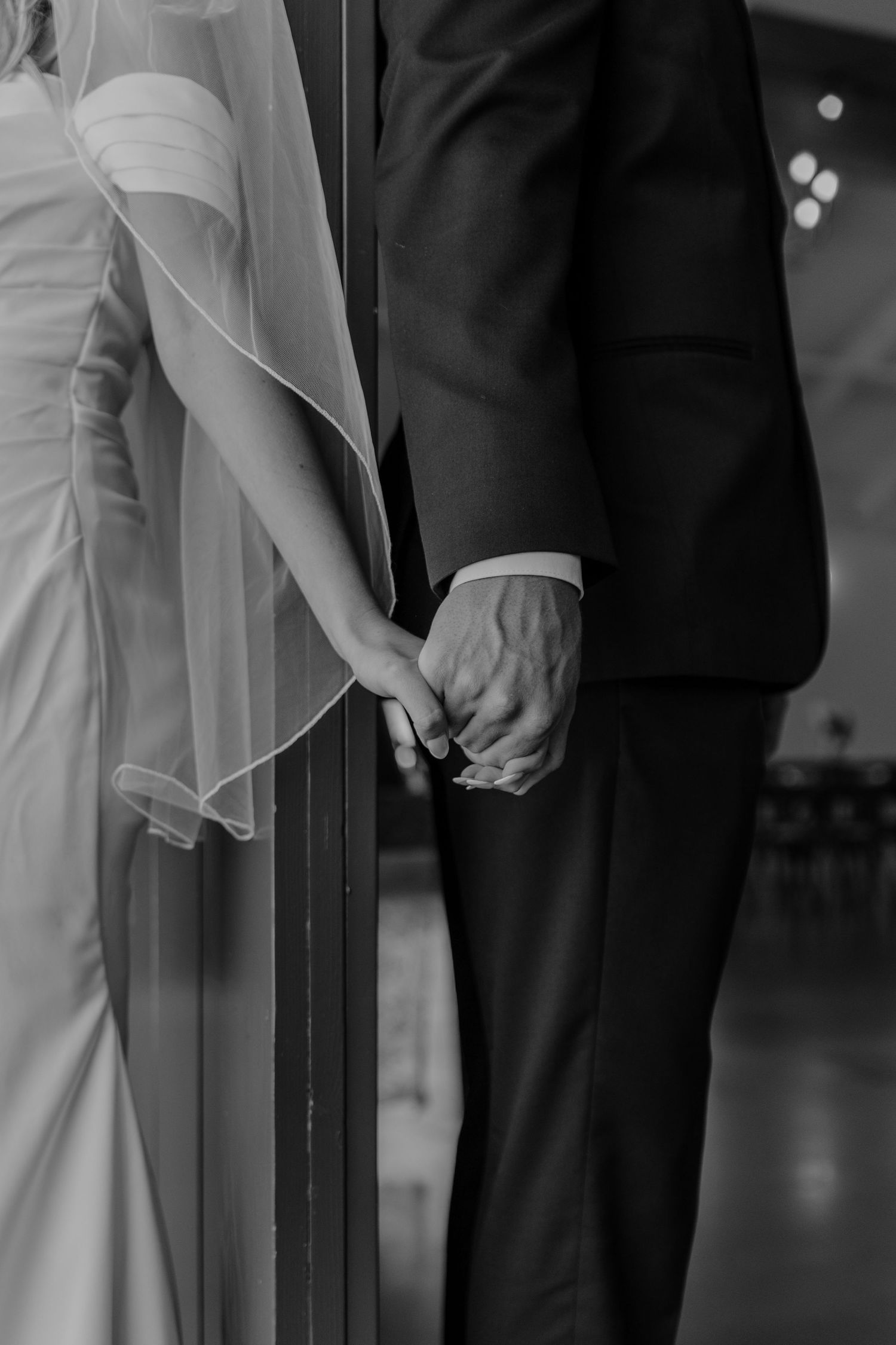 Black and white close-up of bride and groom holding hands during their wedding ceremony.