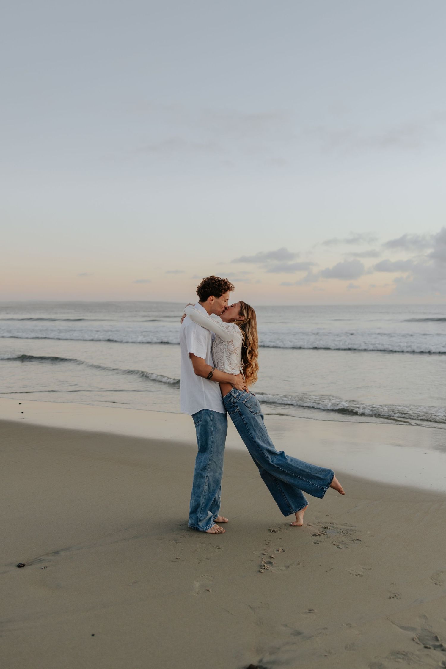 Romantic couple embracing and kissing on beach at sunset with ocean waves.