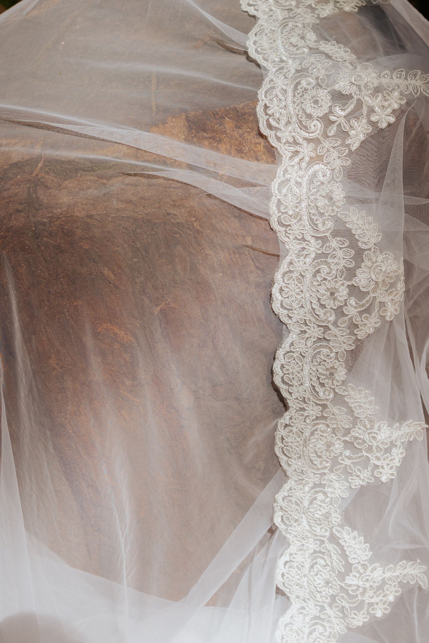 Delicate white bridal veil with intricate lace trim draped over rustic stone surface.