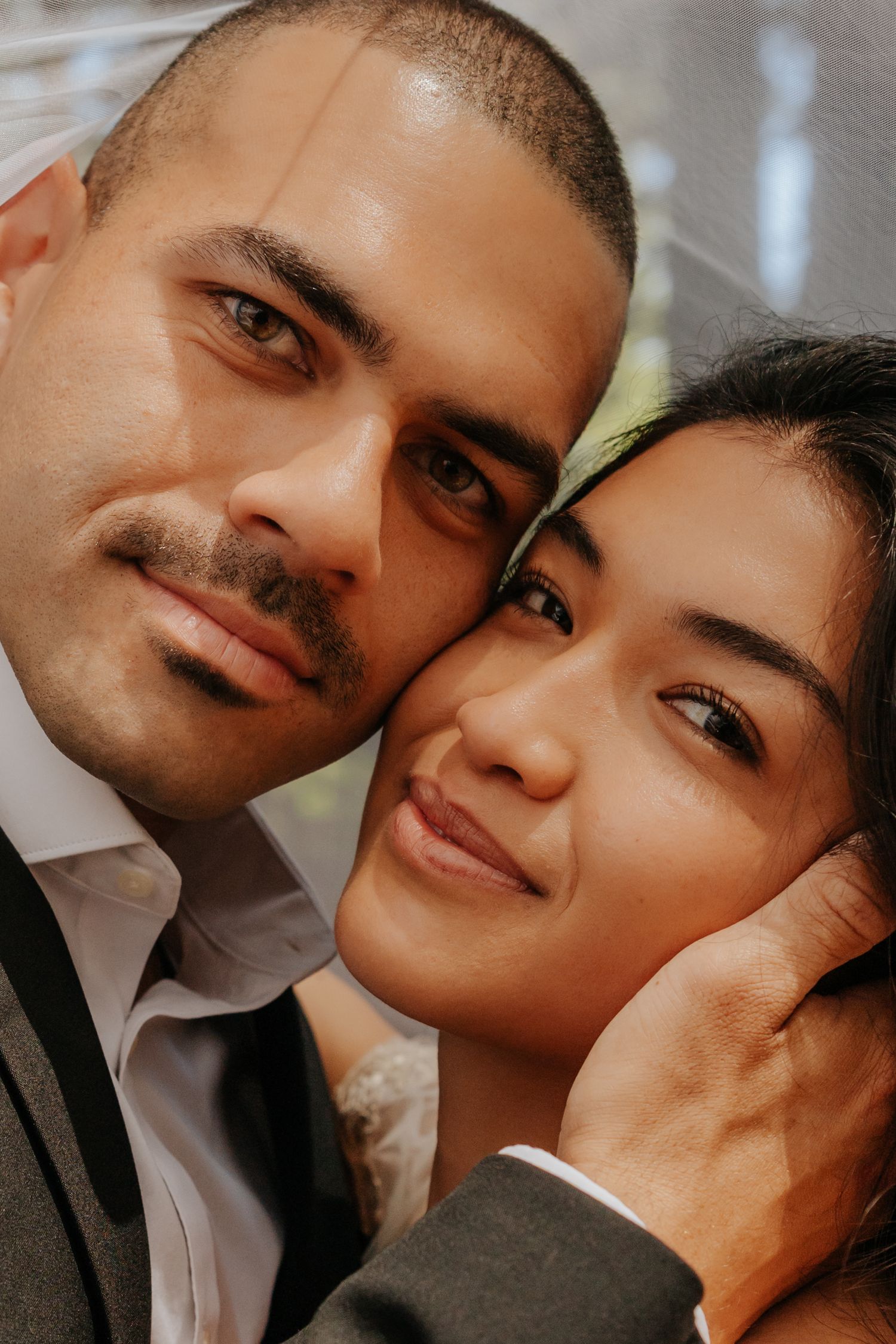Intimate close-up portrait of bride and groom cheek to cheek, groom tenderly holding bride's face.