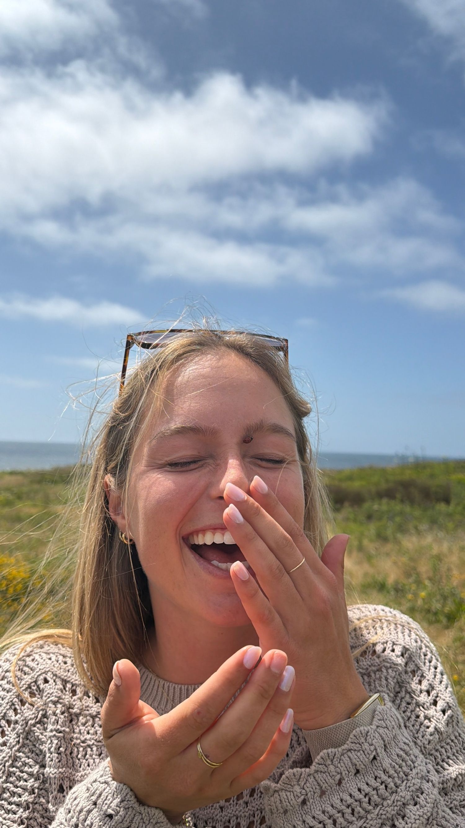 Laughing blonde woman outdoors with sunglasses on head holding white cream in hands.