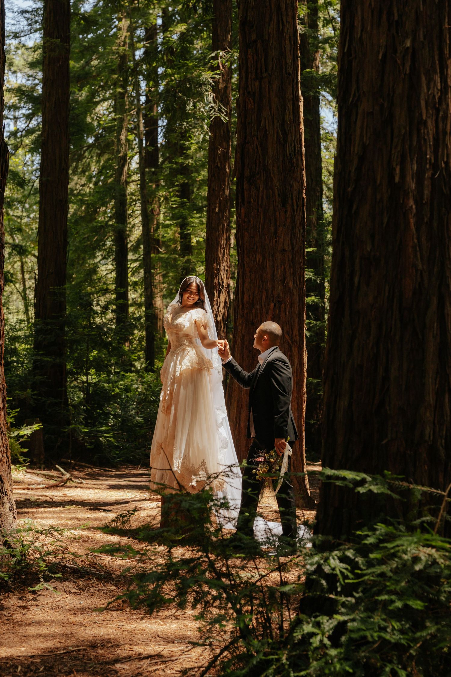 Couple sharing intimate moment during forest elopement ceremony among towering redwood trees.