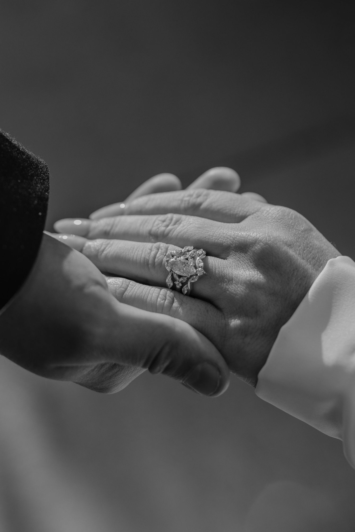 Close-up black and white photo of bride and groom holding hands with ornate diamond wedding ring.