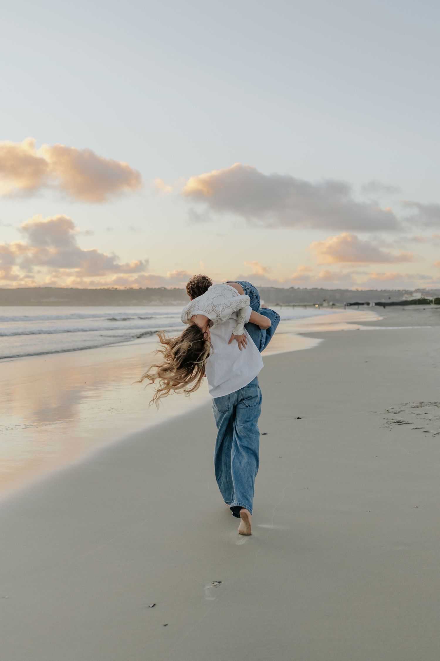 Couple playfully spinning together on sandy beach during golden hour sunset.