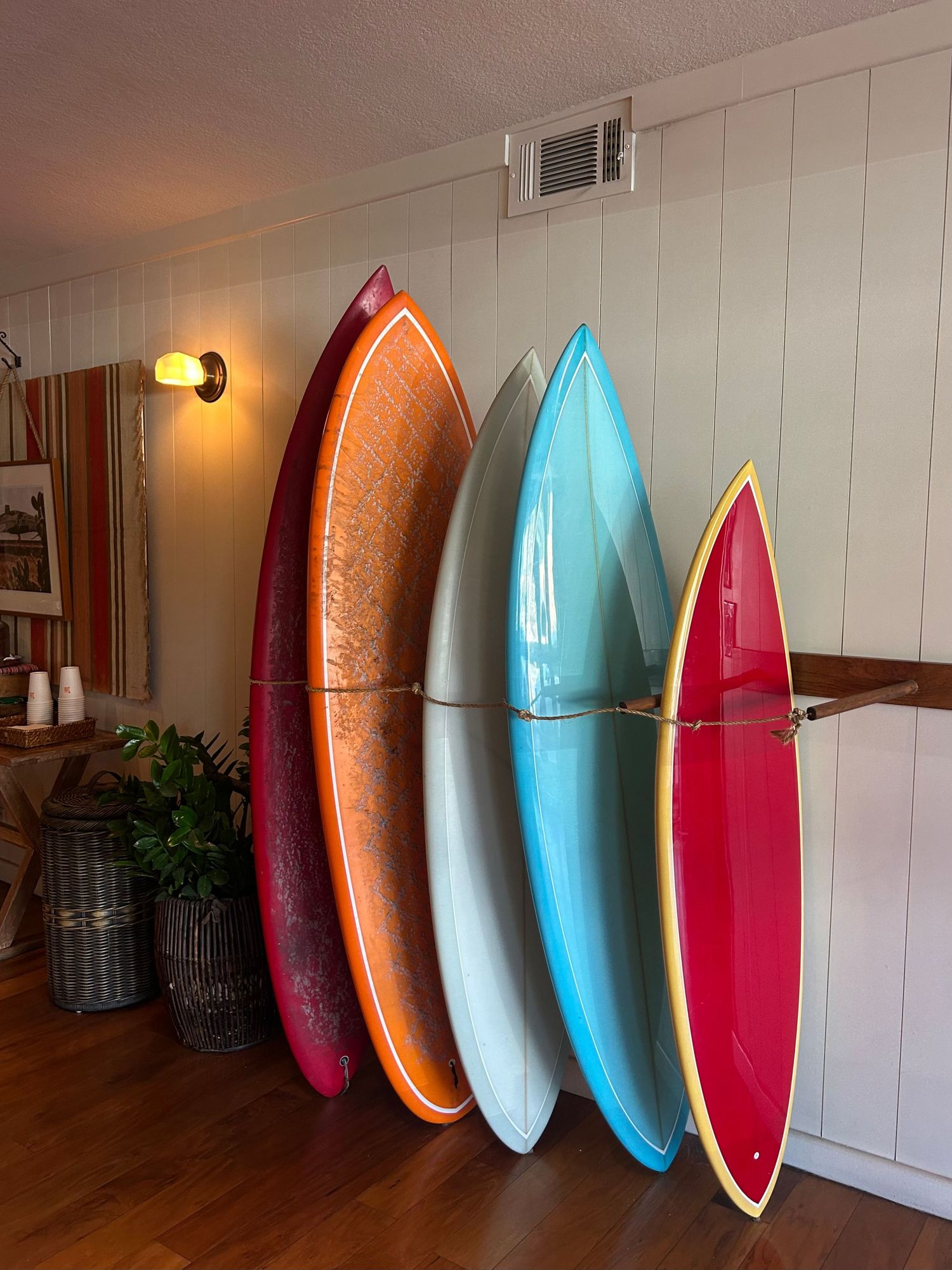Collection of colorful vintage surfboards displayed vertically against a white paneled wall indoors.