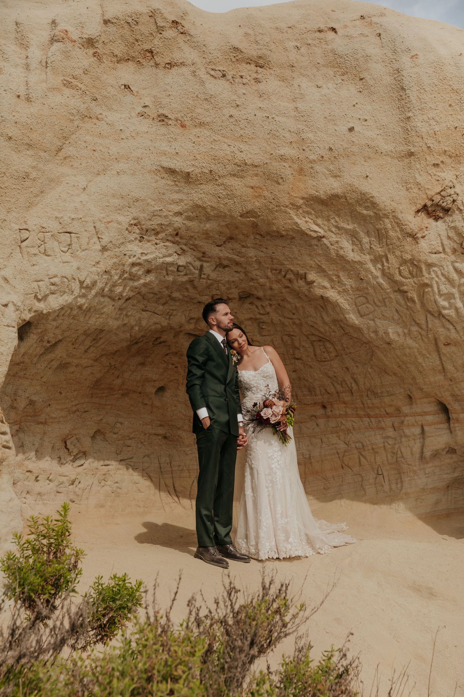 Bride and groom pose romantically inside carved sandstone cave formation at scenic outdoor wedding location.