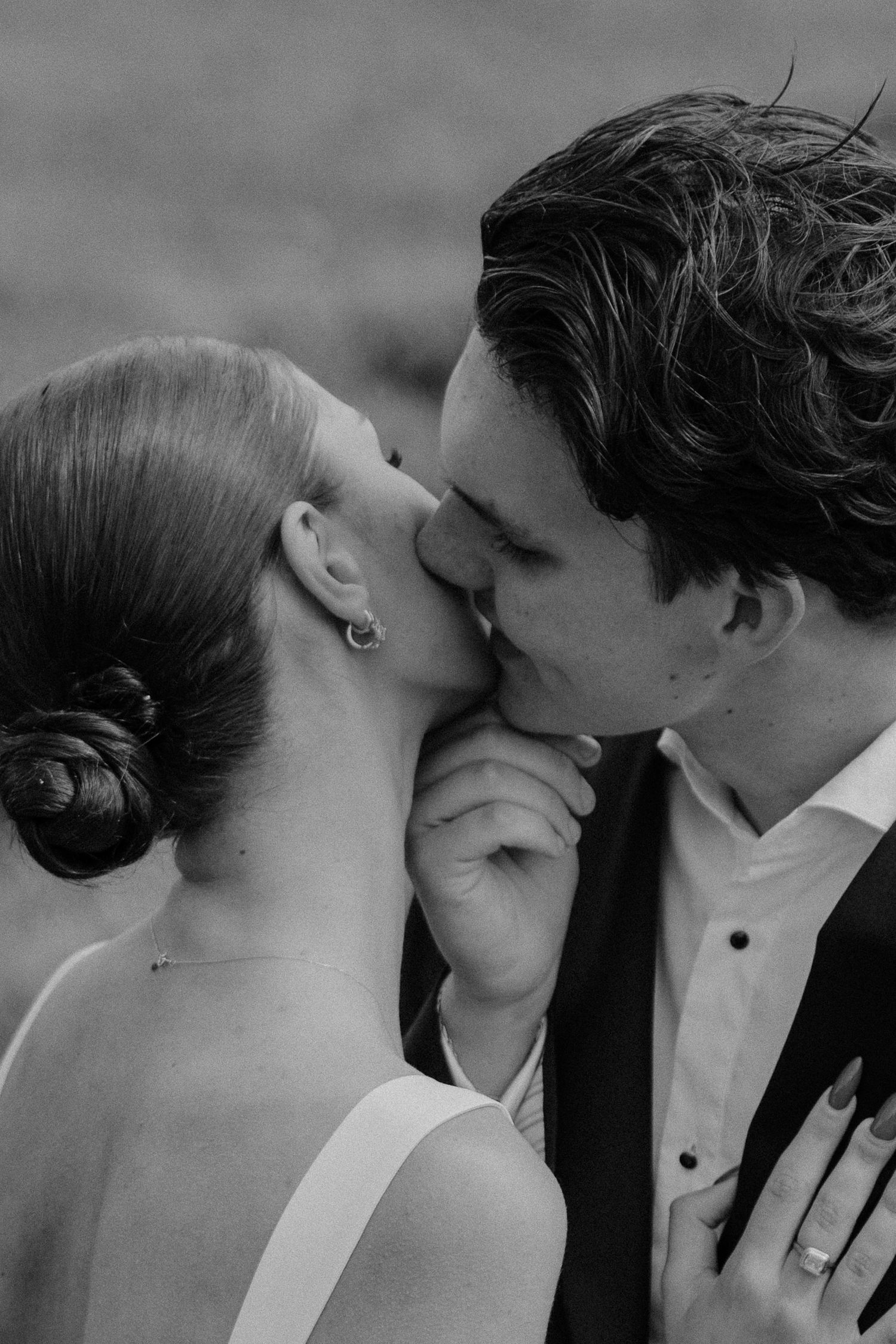 Black and white romantic close-up of couple sharing a kiss, bride wearing elegant updo and drop earring.