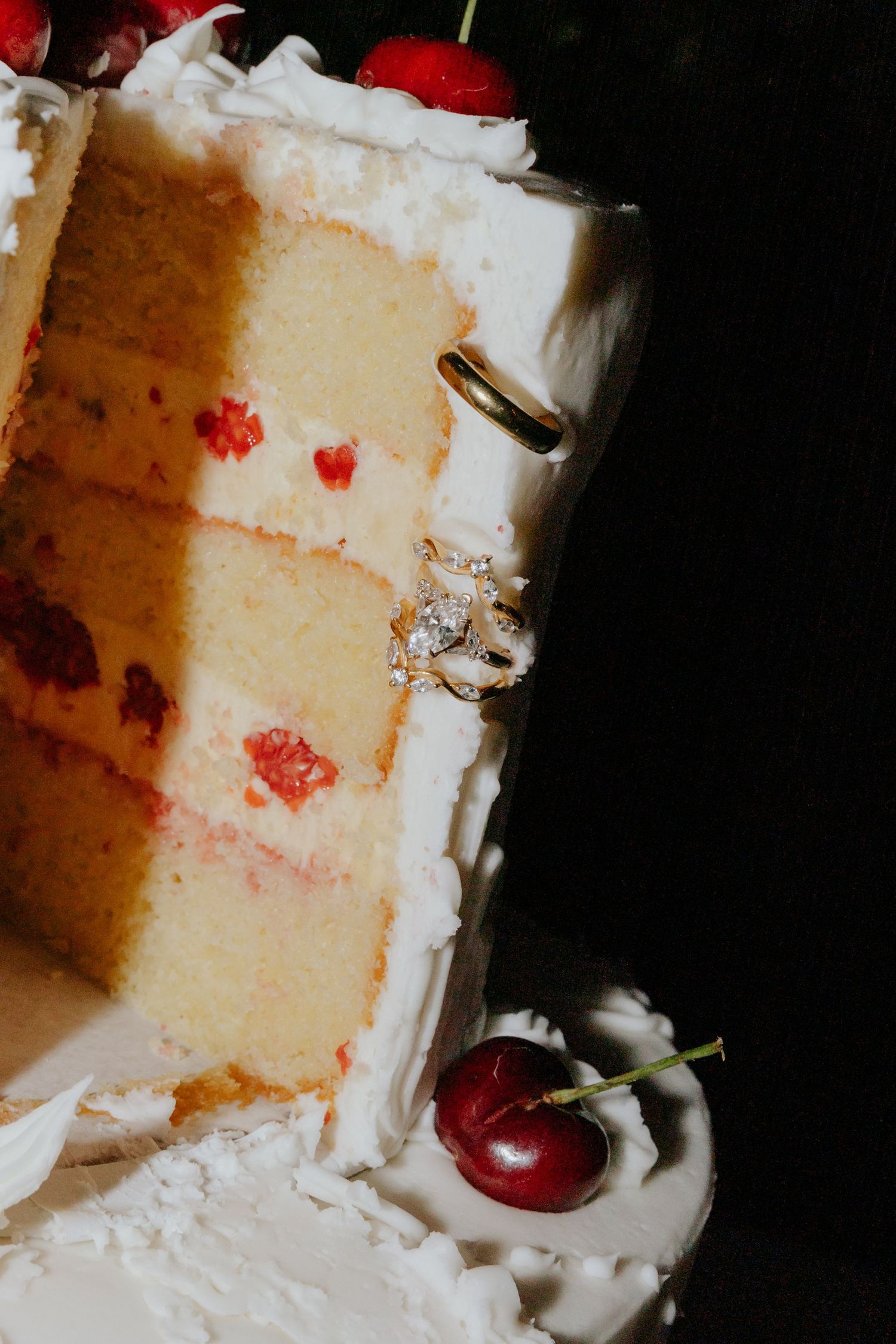 Close-up of sliced white wedding cake with cherries and diamond engagement ring displayed on frosting.