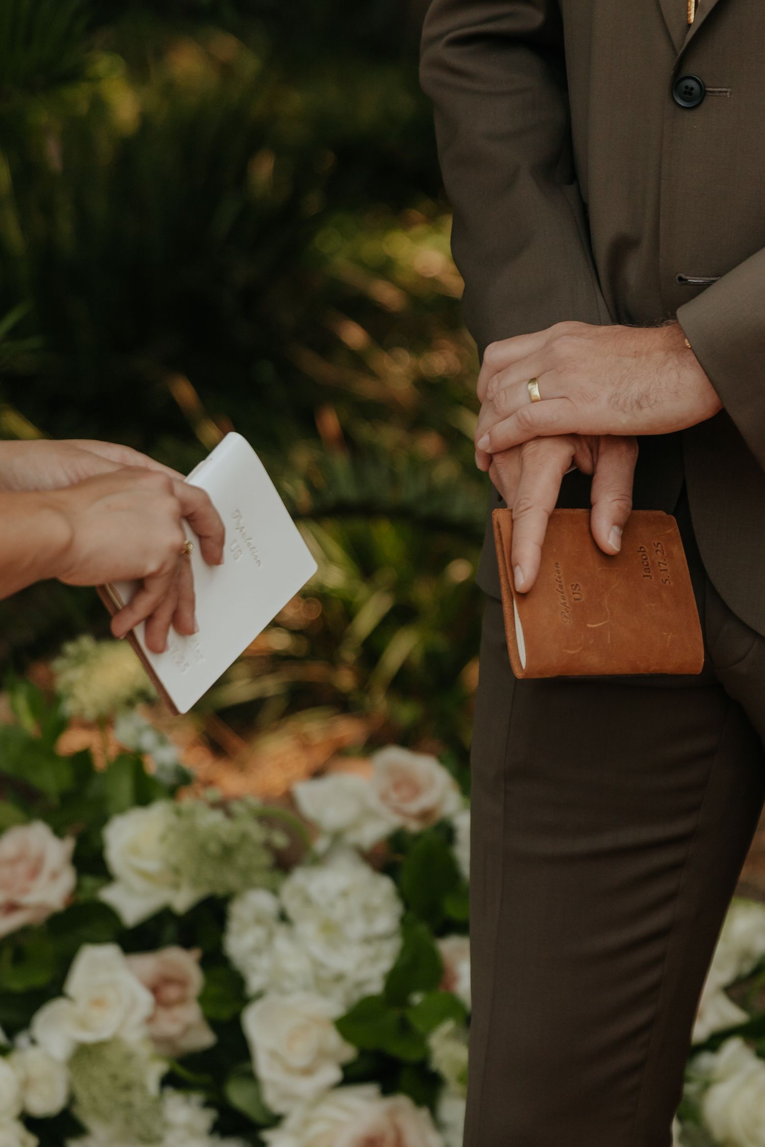 Officiant holds leather book while receiving vow notes during an outdoor garden wedding ceremony.
