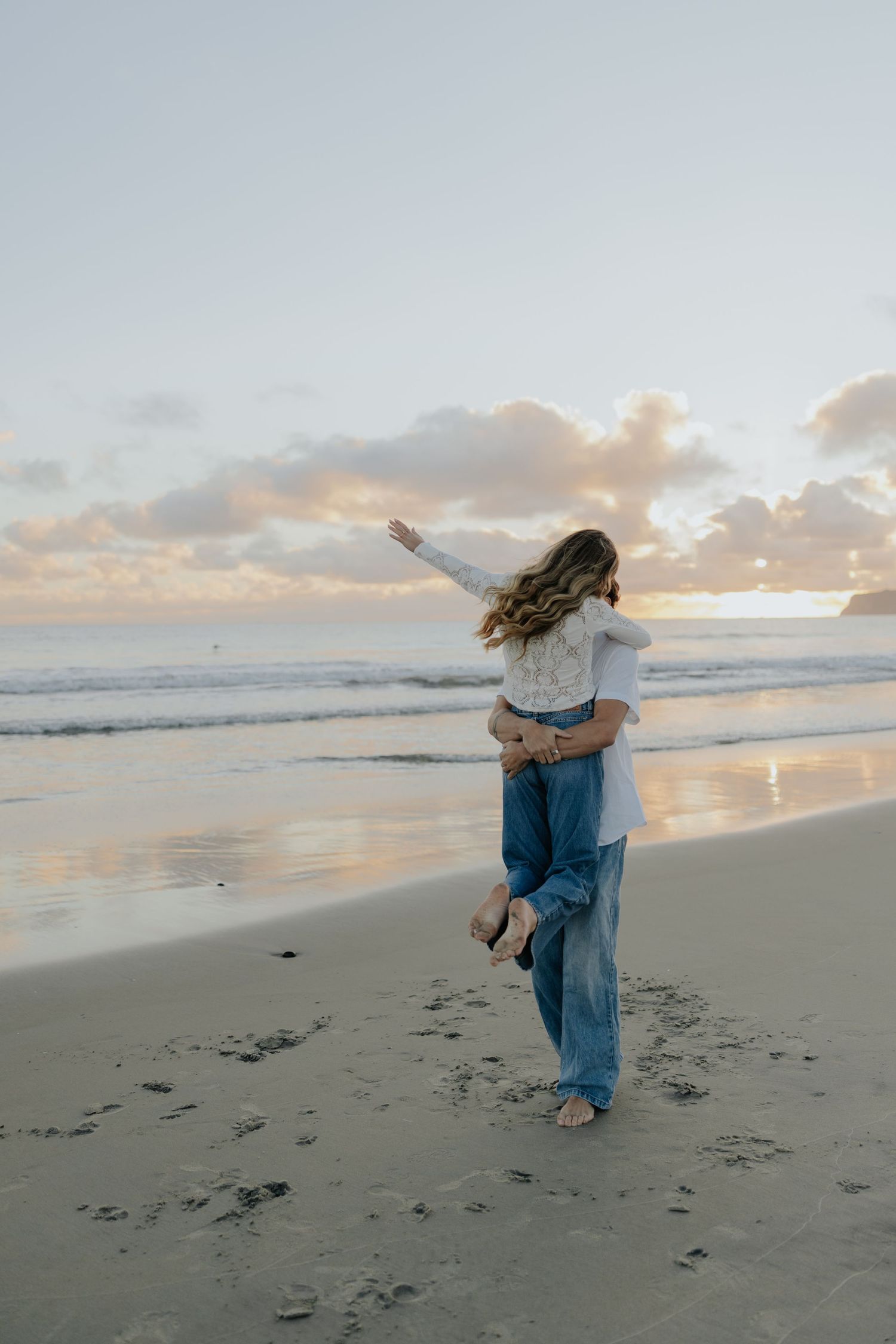 Couple sharing romantic moment at sunset beach, woman lifted with arms outstretched.
