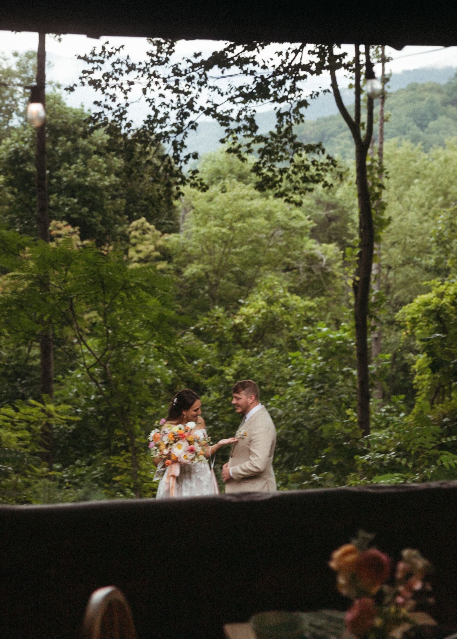 Couple exchanging vows on an open-air venue overlooking a lush green forest valley.