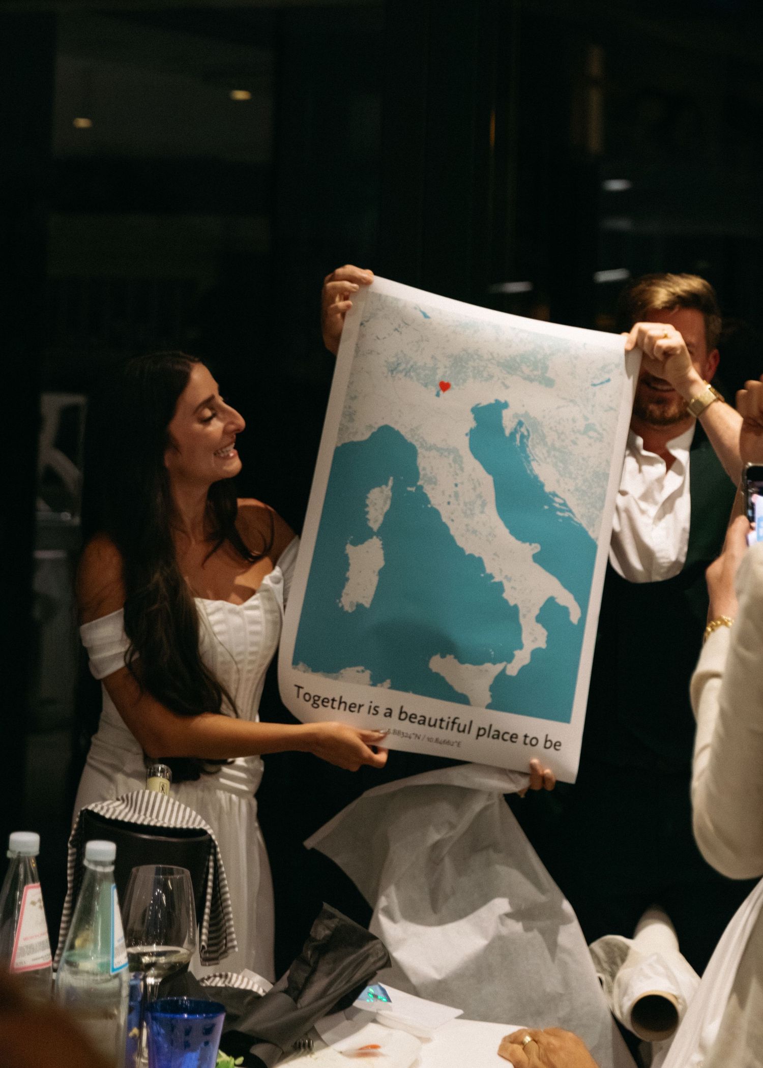 Bride smiles while holding a map of Italy poster reading Together is a beautiful place to be.