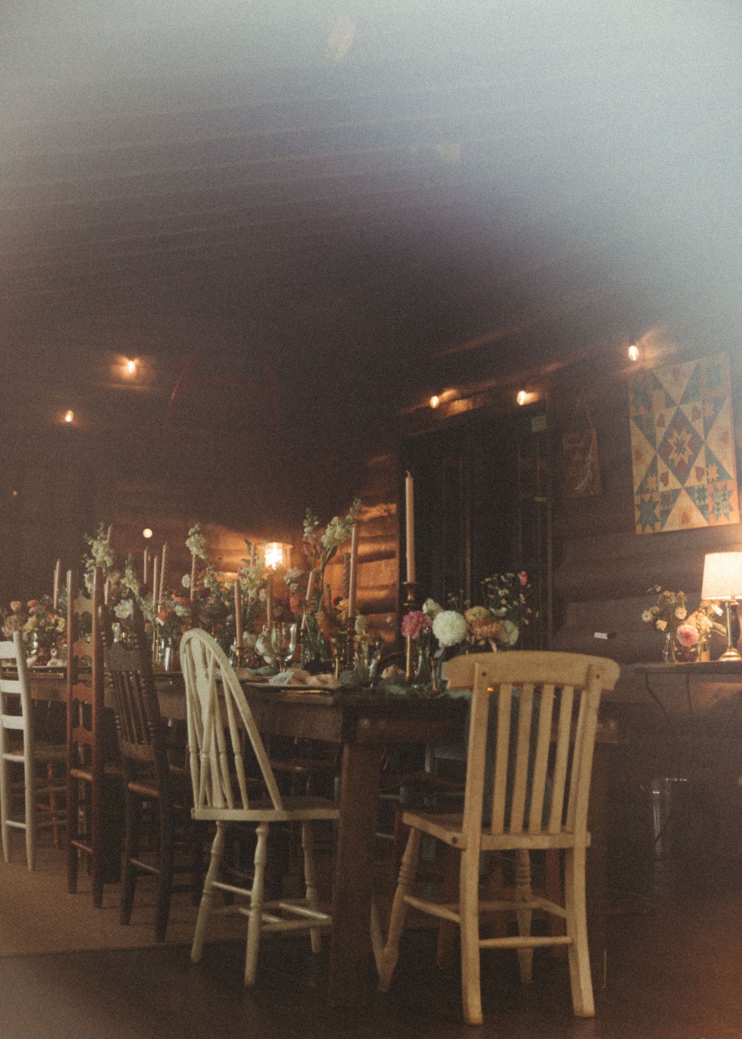 Long wooden dining table set with flowers and candles in a dark rustic cabin reception hall.