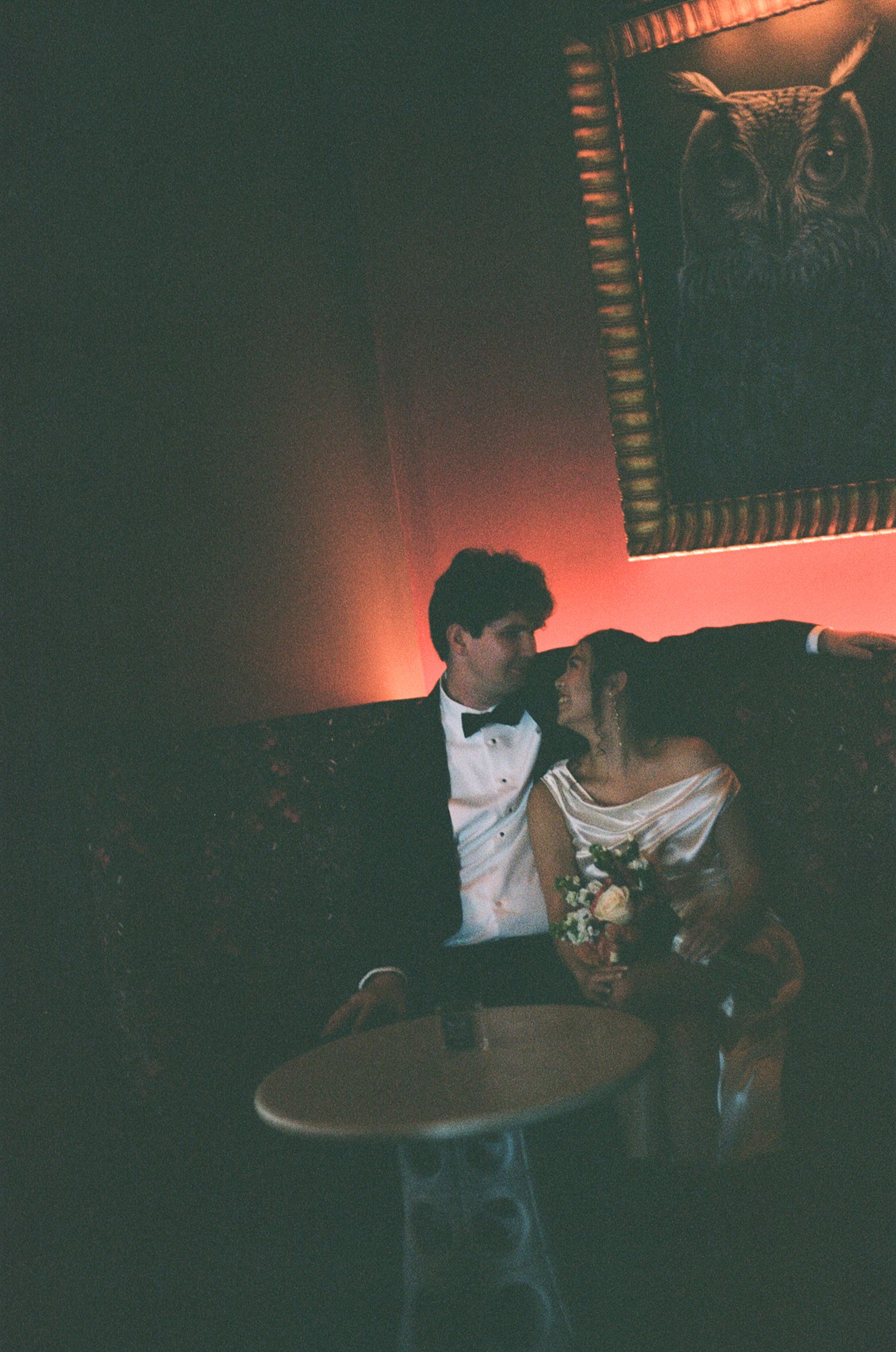Bride and groom in wedding attire sharing an intimate moment in a dimly lit romantic bar.