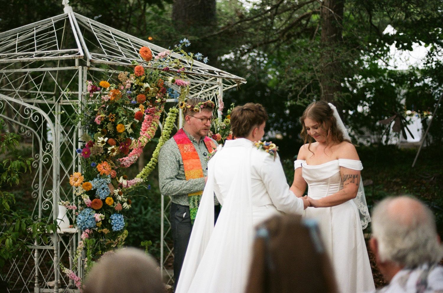 White lace bridal veil and blue floral pointed-toe heels displayed against green leafy hedge.