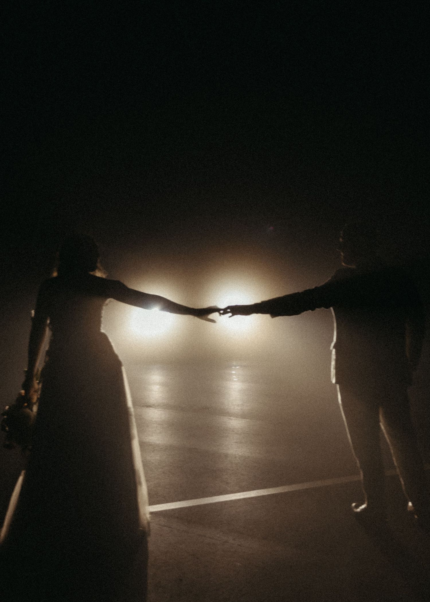 Silhouette of bride and groom reaching toward each other in foggy parking lot at night.