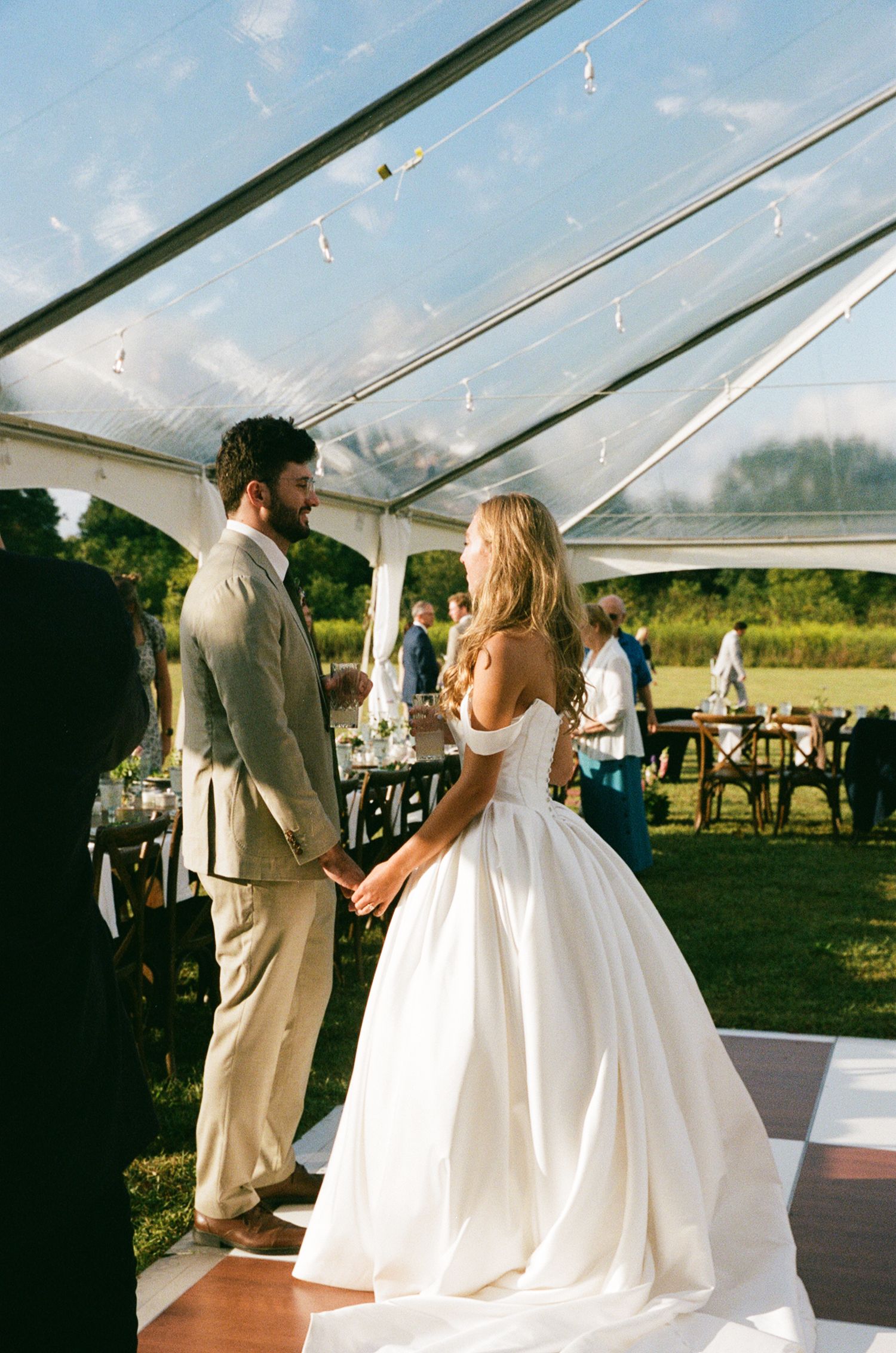 Bride and groom share first dance under clear reception tent at golden hour outdoor farm wedding.