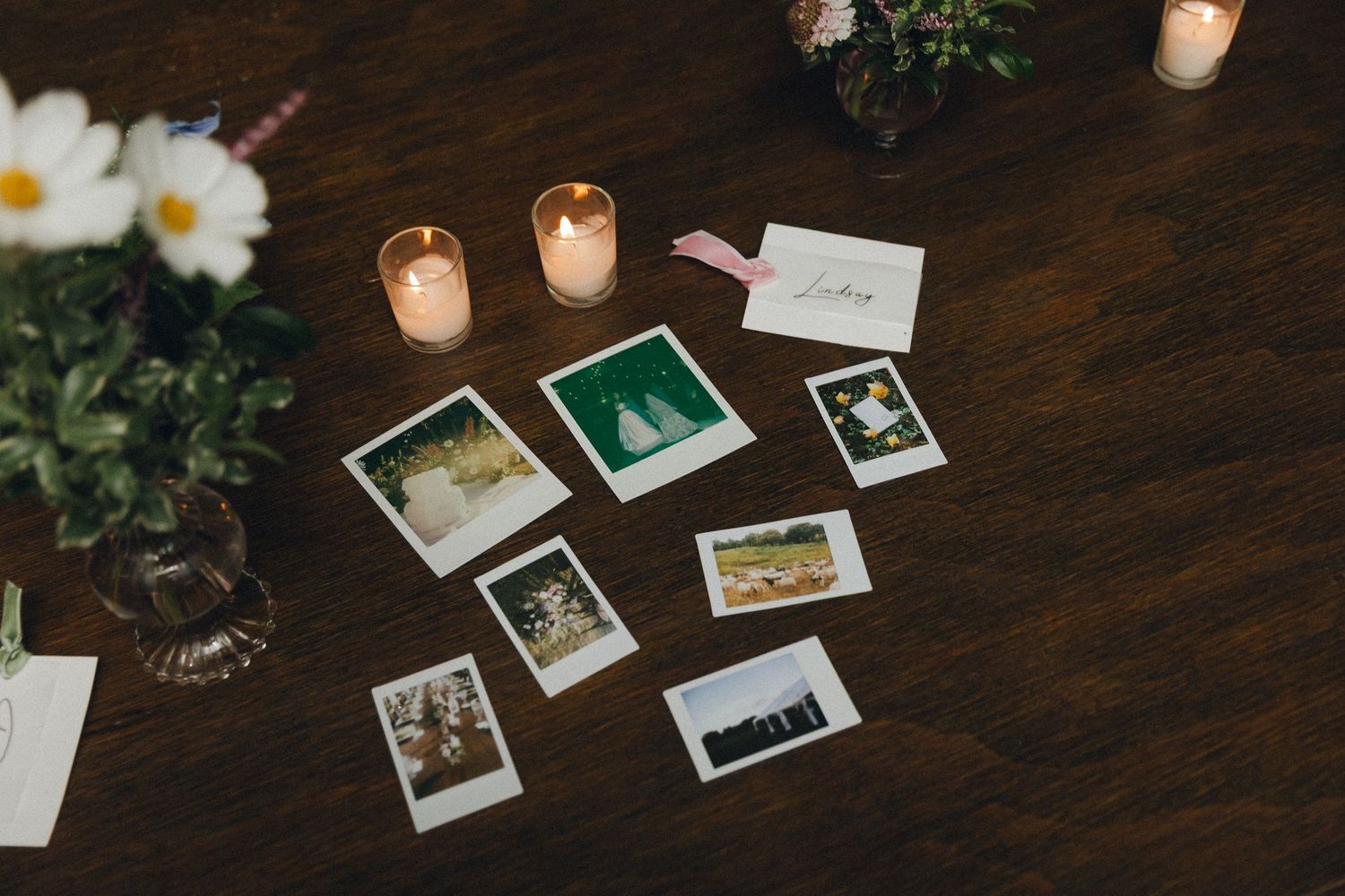 Polaroid photos, candles, and flowers arranged on a wooden table as wedding reception decor.