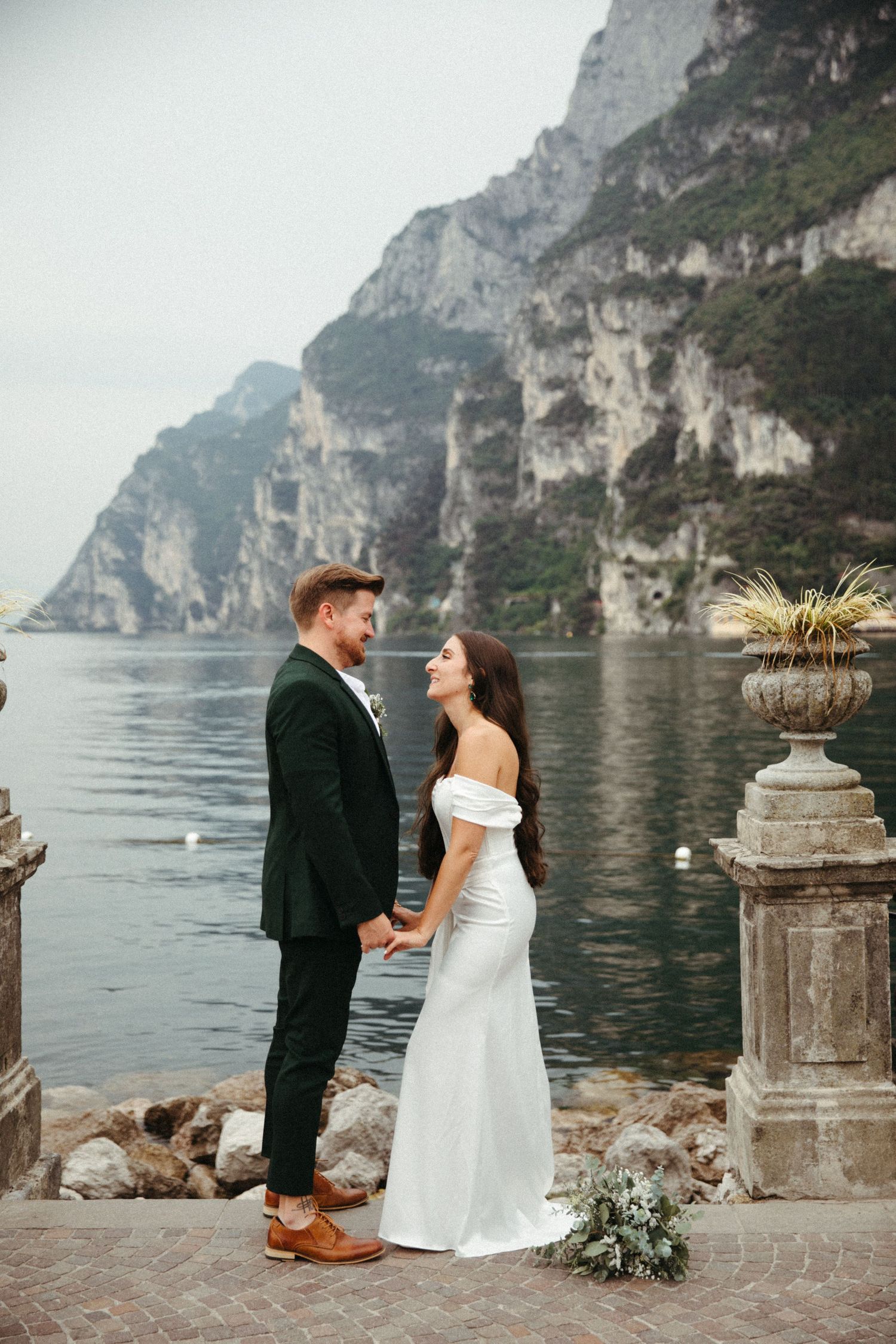 Bride and groom hold hands facing each other by a stunning mountain lake wedding venue.