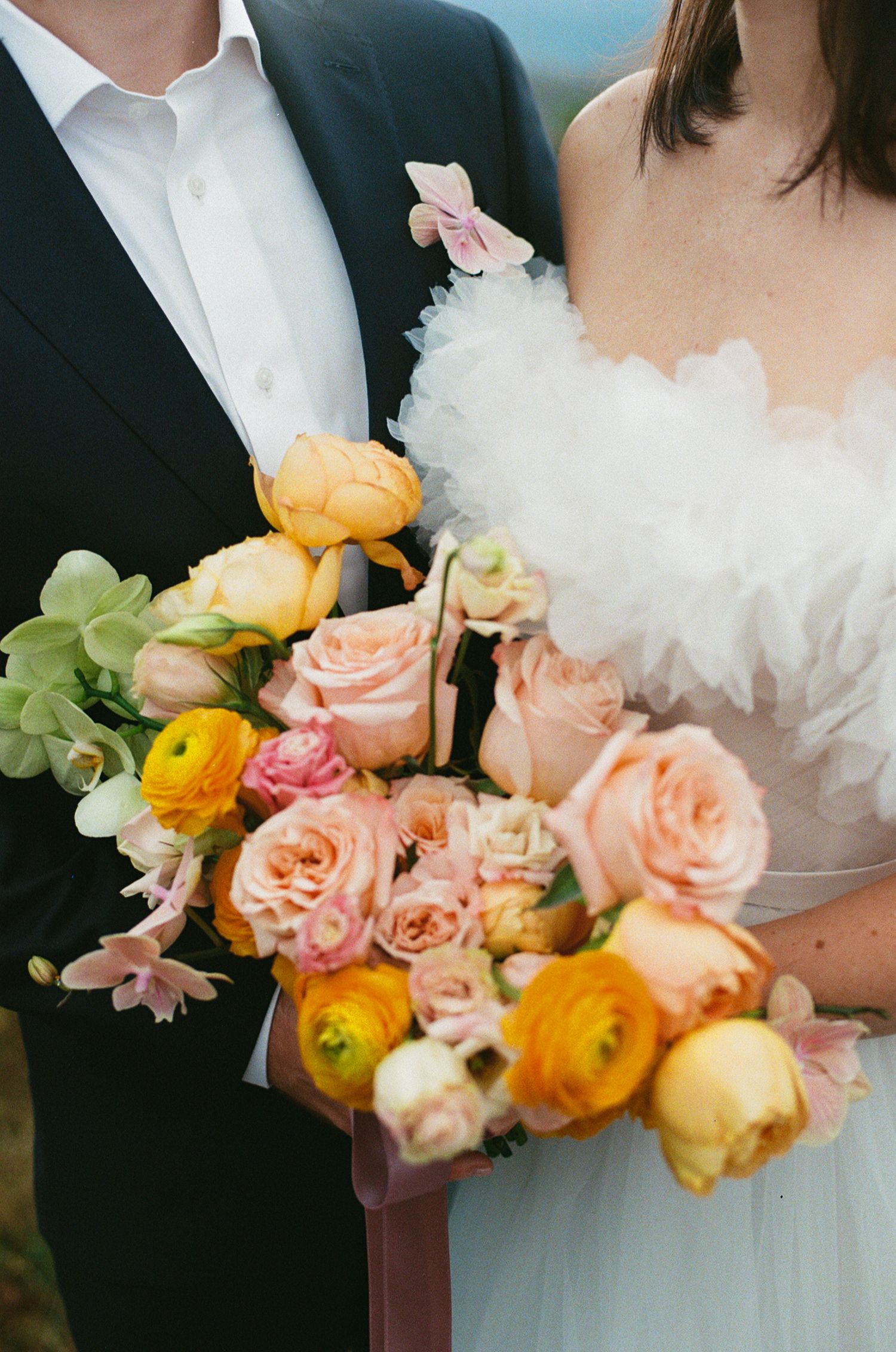 Close-up of a vibrant wedding bouquet featuring peach roses, orange ranunculus, and green hydrangea blooms.