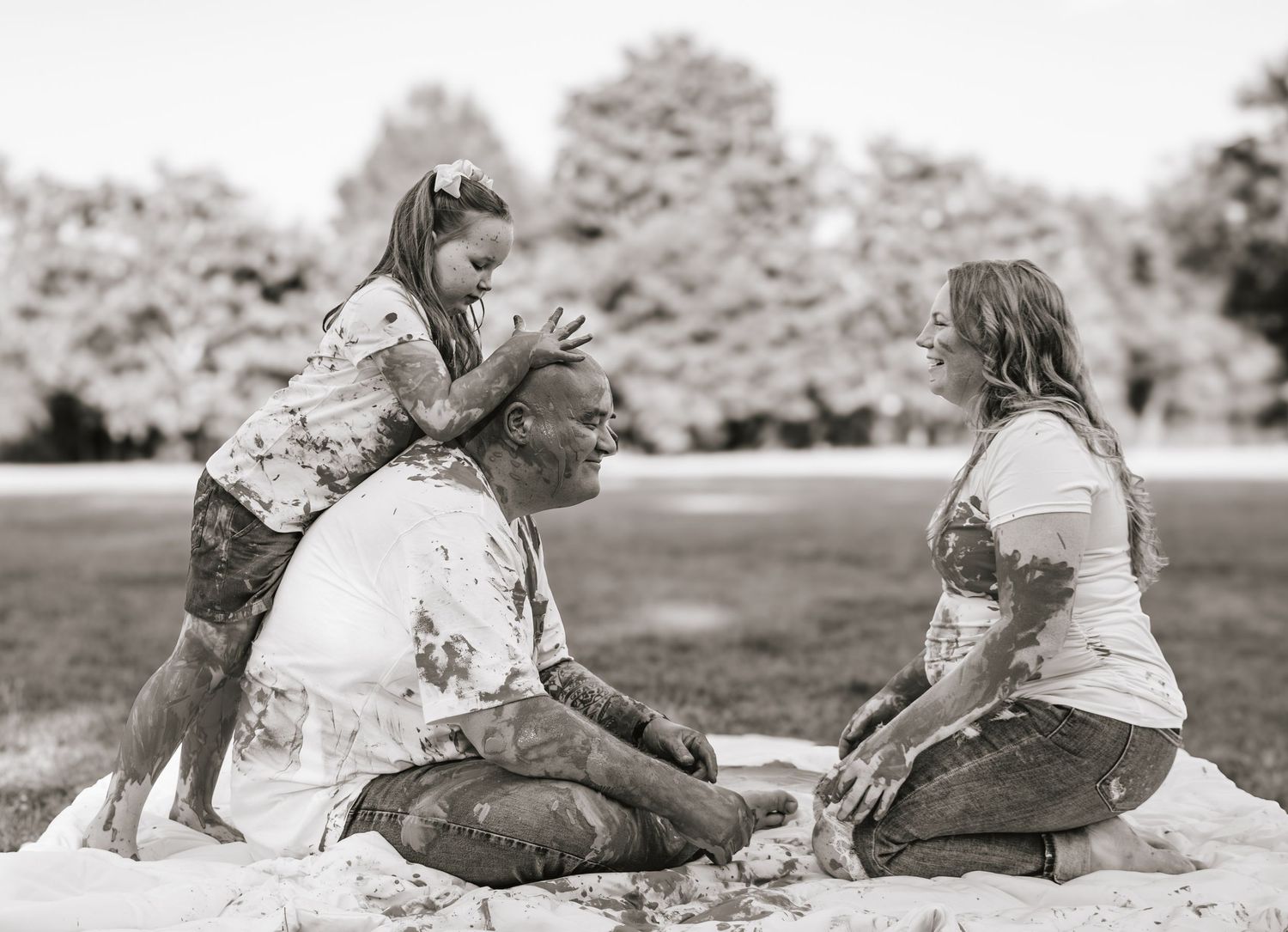 Black and white photo of a family playing together outdoors, covered in paint, sharing a joyful moment.