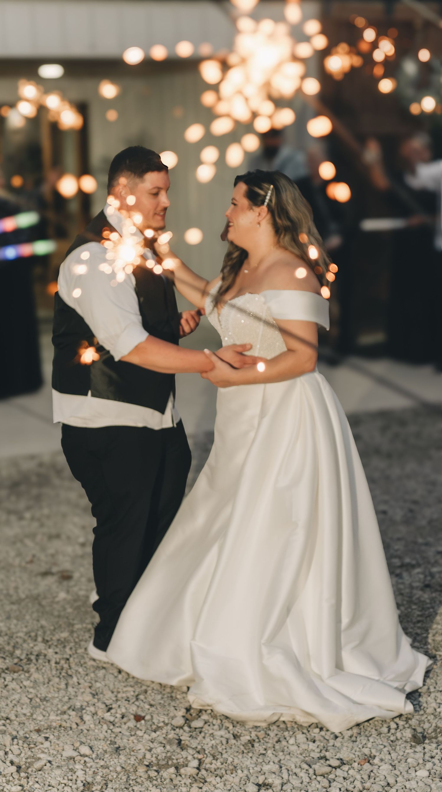 Bride and groom share romantic first dance surrounded by glowing sparklers at outdoor wedding reception at night.