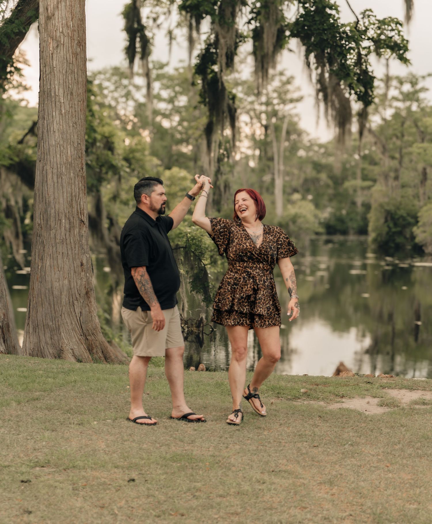 Laughing couple dancing together near a cypress lake surrounded by Spanish moss-draped trees.
