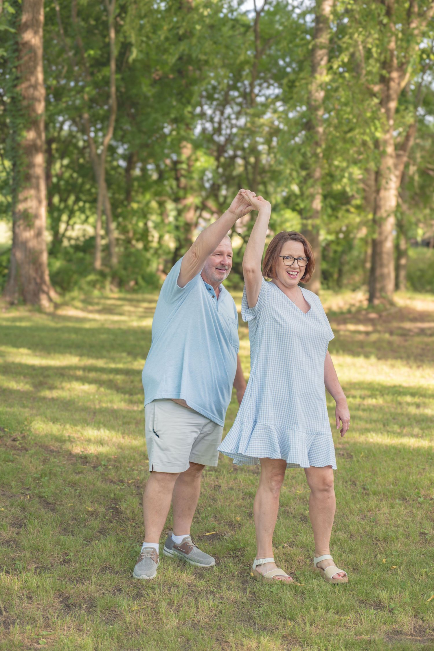 Happy couple in matching light blue outfits dancing together in sunny green park.