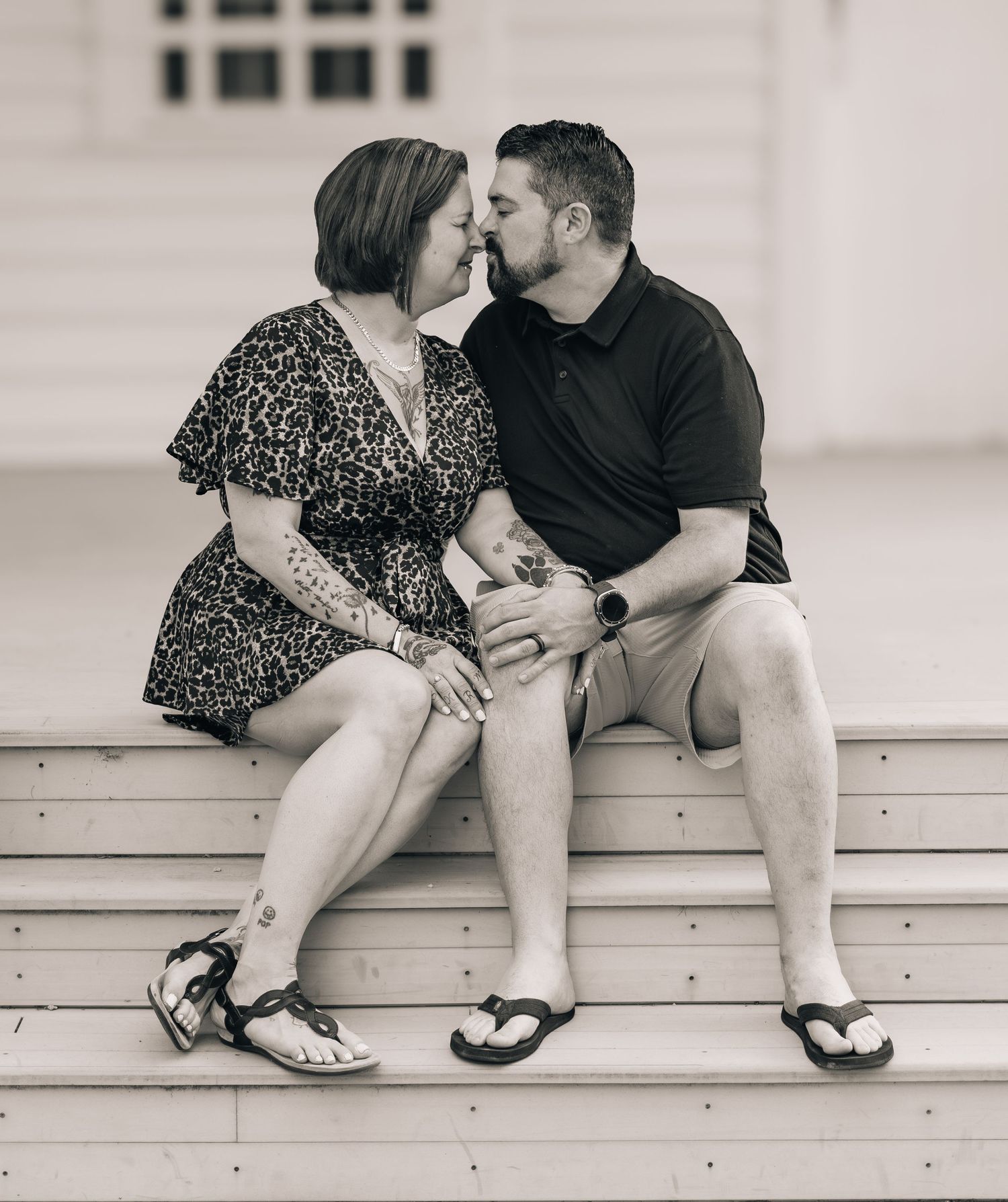 Black and white photo of a couple sharing a kiss while sitting on wooden steps outdoors.