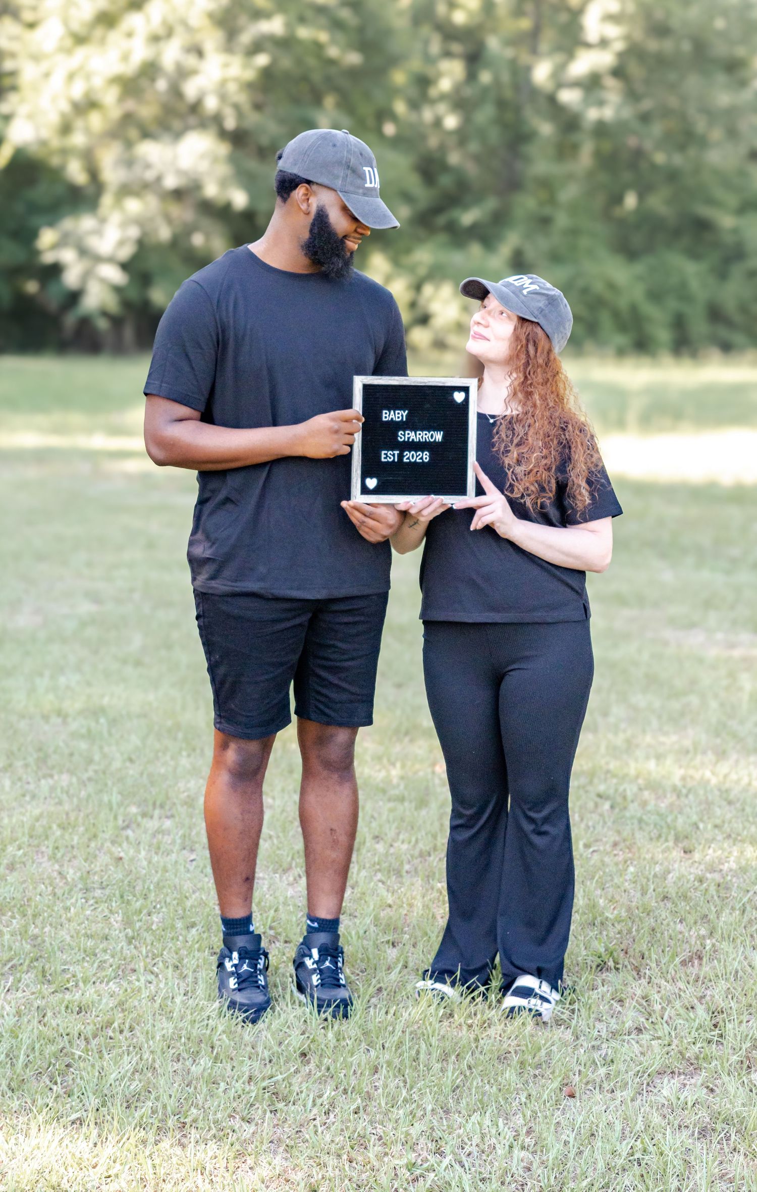 Couple holding Baby Sparrow Est 2026 letterboard sign standing together in a sunny green park.