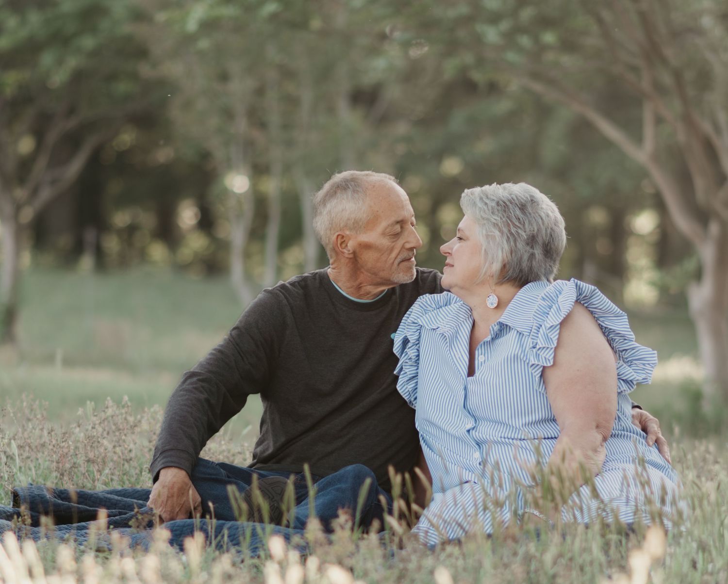 Elderly couple sitting together in tall grass field sharing a tender moment outdoors.