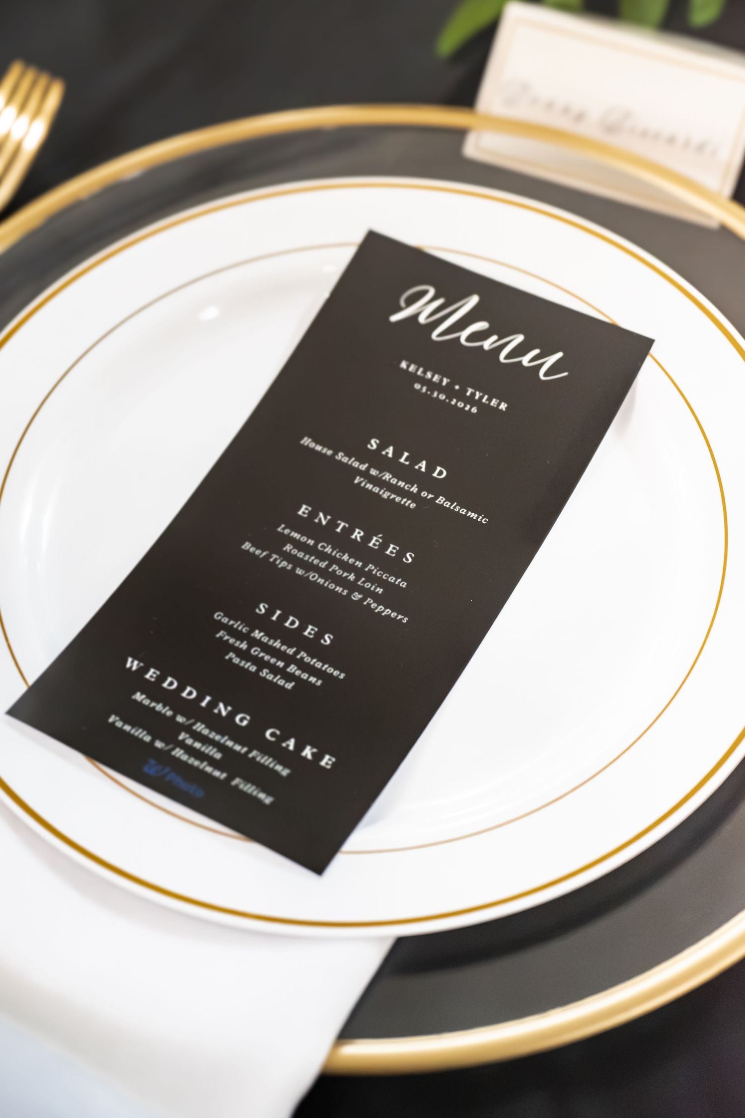 Elegant wedding menu card on white and gold plate with black background and white script font.