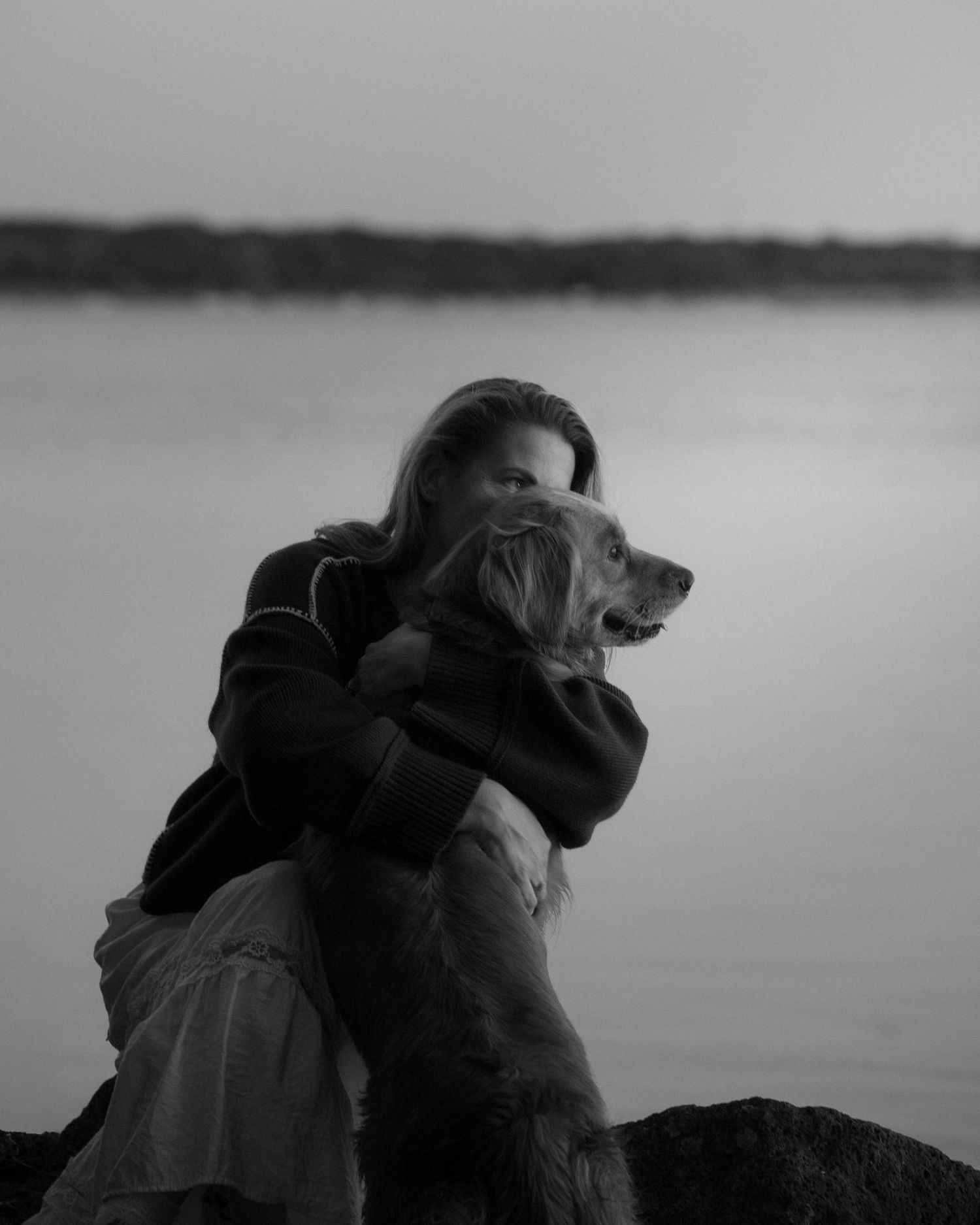 Woman hugging her golden retriever dog by a lake in black and white photo.