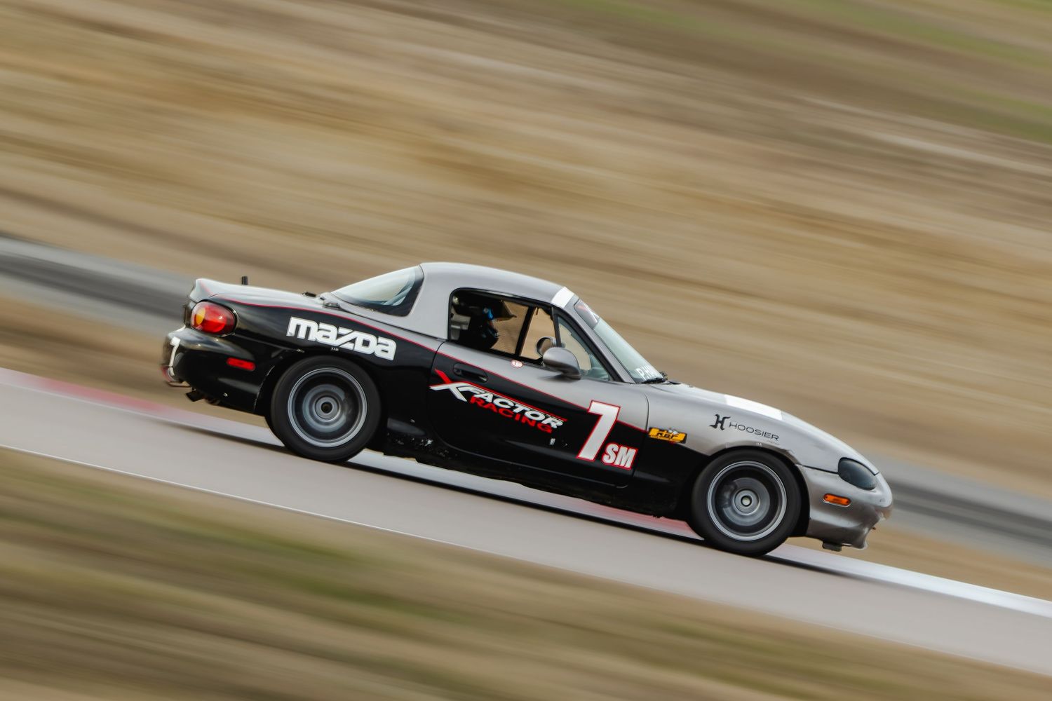 Mazda MX-5 number 7 races on track with motion blur.