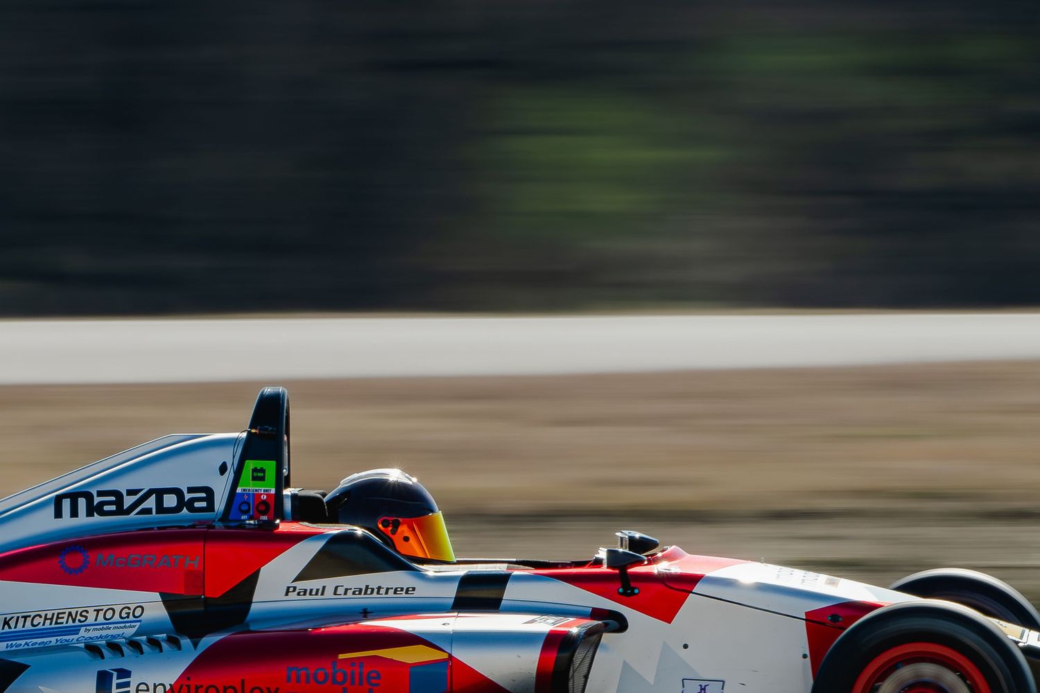 Formula Mazda race car with driver Paul Crabtree speeding on track with motion blur background.