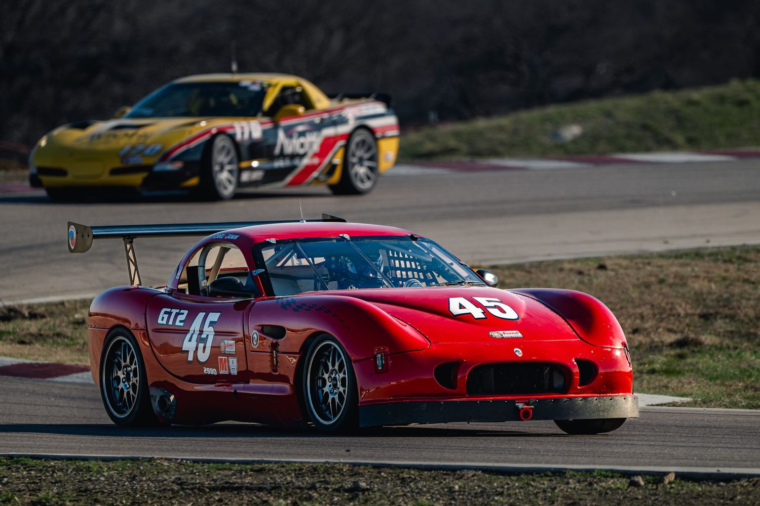 Red Panoz car number 45 leads a yellow Corvette on a race track.