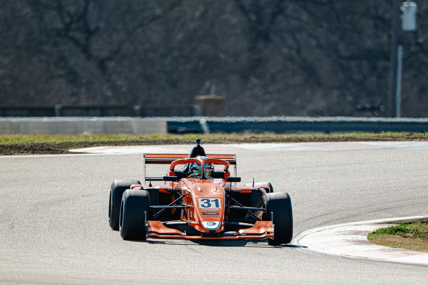 Orange Formula 3 race car number 31 speeding on a circuit track during a motorsport competition.